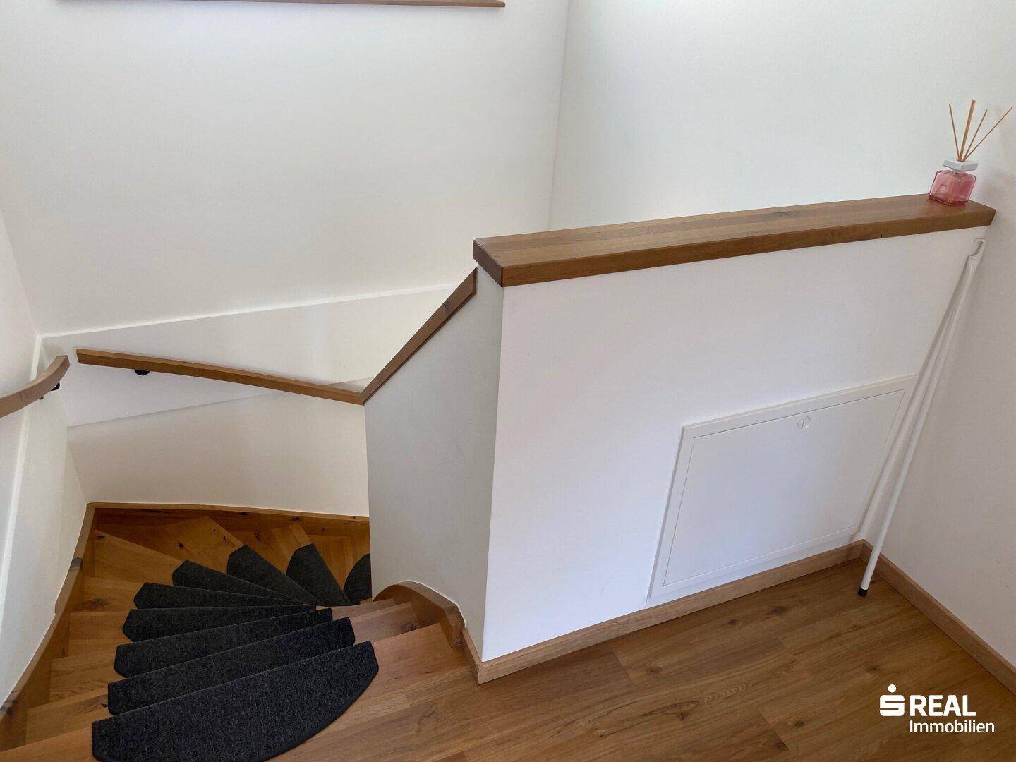 Treppenaufgang mit Holzstufen und weißem Geländer, führt in die obere Etage.