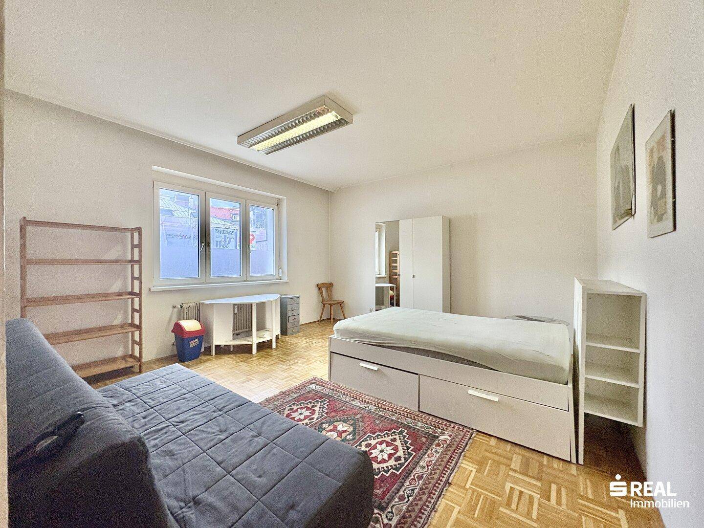 Geräumiges Schlafzimmer mit Parkettboden, Bett und Sofa, ideal für flexible Nutzung.
