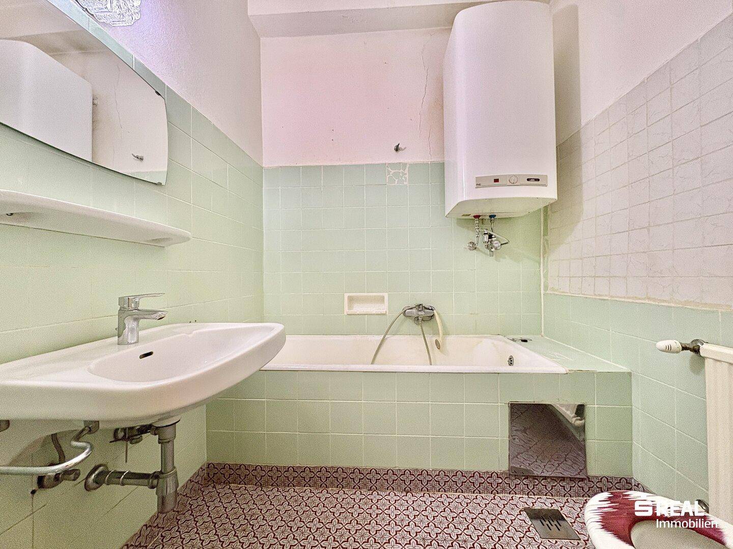 Badezimmer mit mintgrünen Fliesen, Badewanne und Waschbecken, im Stil der 80er Jahre.