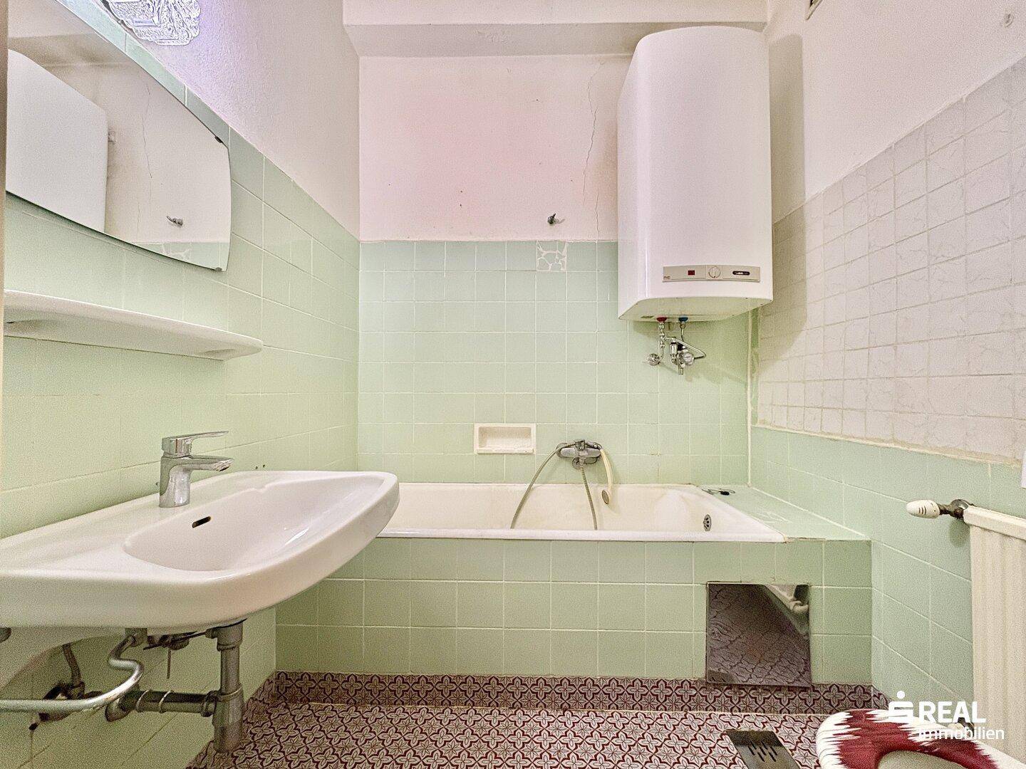 Badezimmer mit Badewanne, Waschbecken und Boiler, gekennzeichnet durch mintgrüne Fliesen.