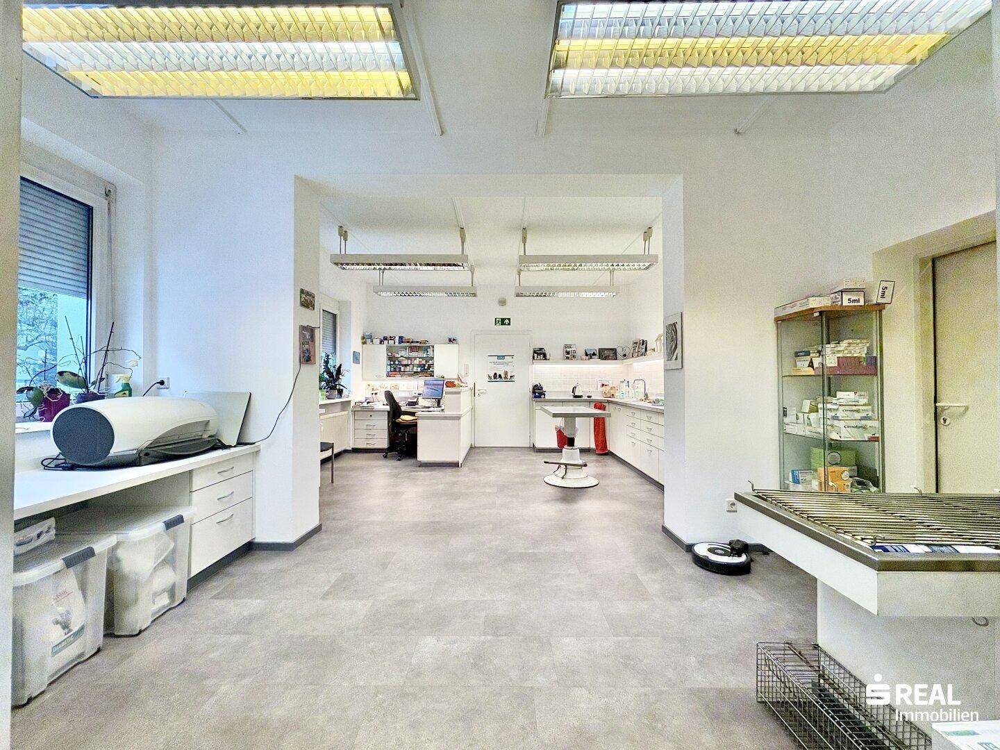 Heller Arbeitsbereich mit Schreibtischen, Untersuchungsbank und Blick auf weitere Funktionsräume.