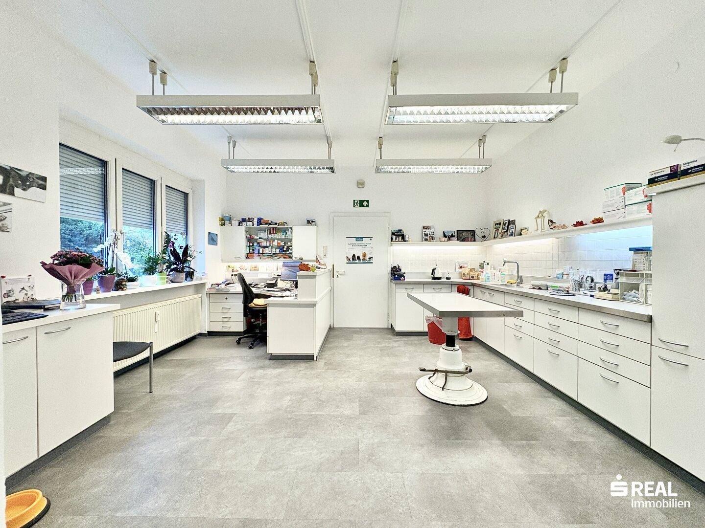 Großer Arbeitsraum mit langen Arbeitsflächen, Schränken und einem Behandlungstisch.