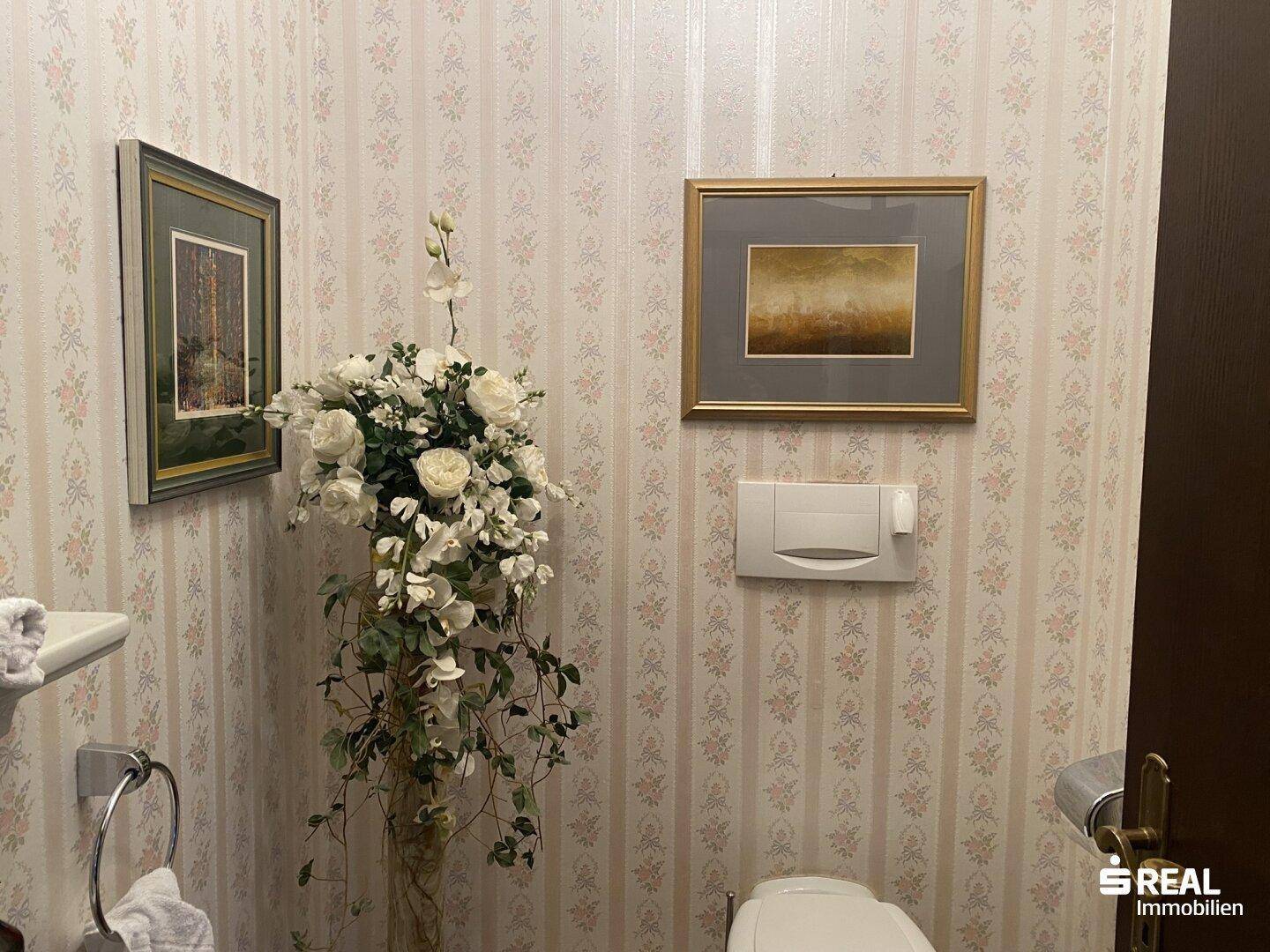 Charmantes Gäste-WC mit floraler Tapete und einer eleganten Blumendekoration.