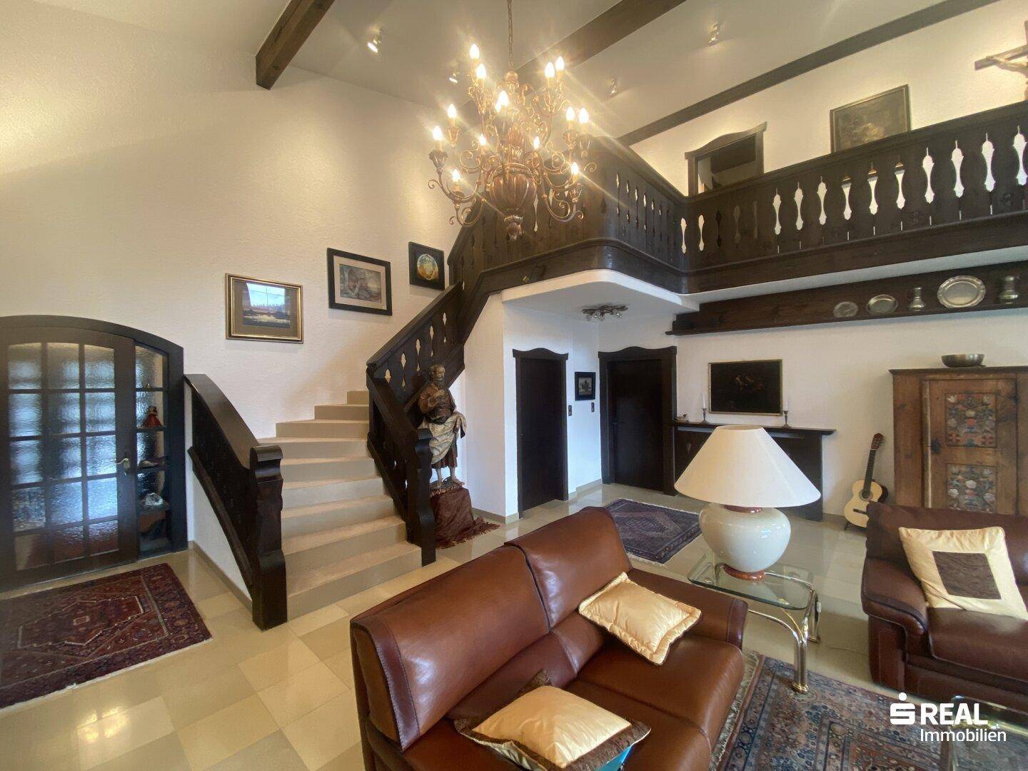 Großzügiger Wohnbereich mit traditioneller Holztreppe, Ledersofas und einem opulenten Kronleuchter.