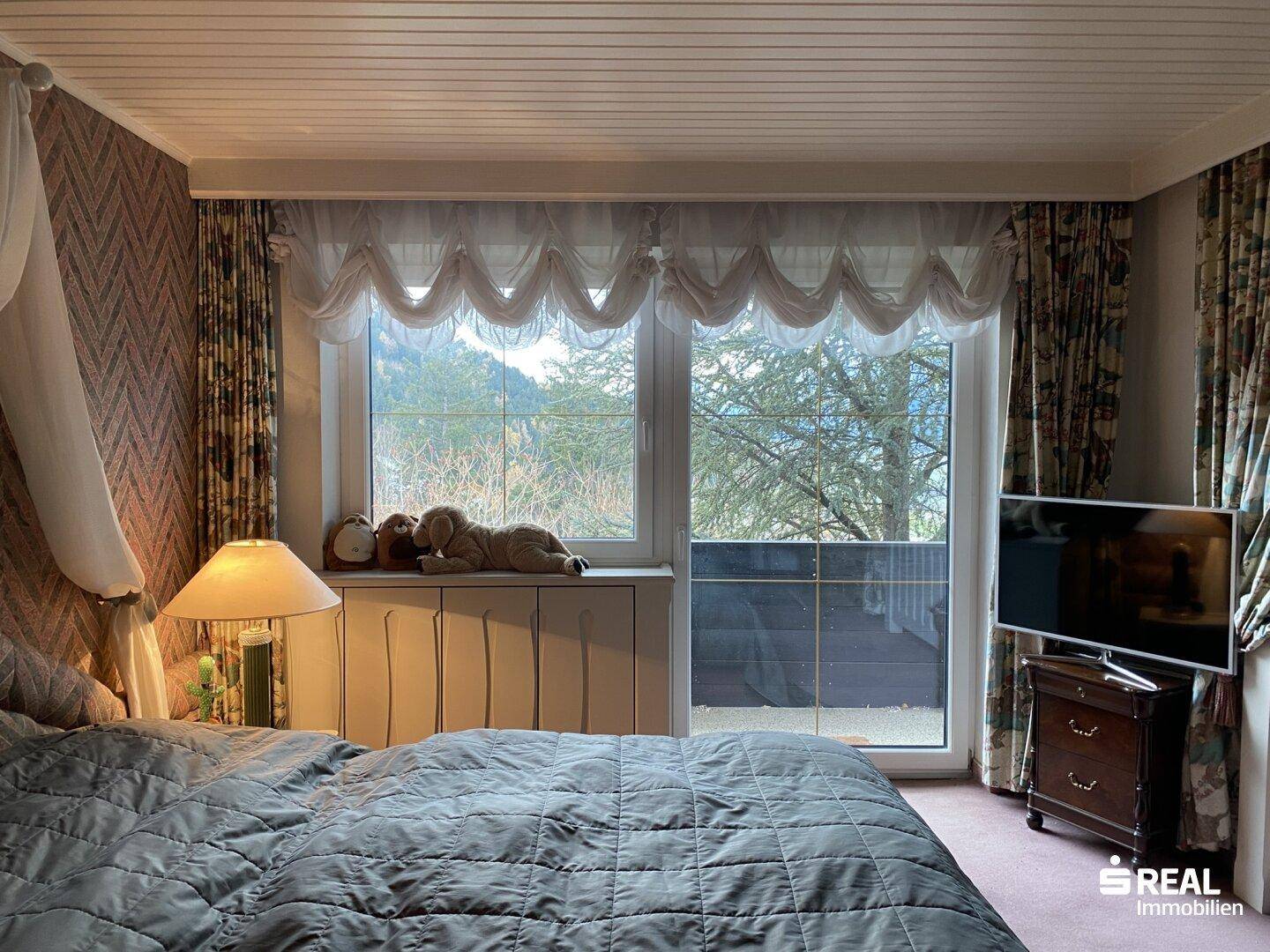Gemütliches Schlafzimmer mit großem Fenster, das einen weiten Blick in die grüne Landschaft bietet.