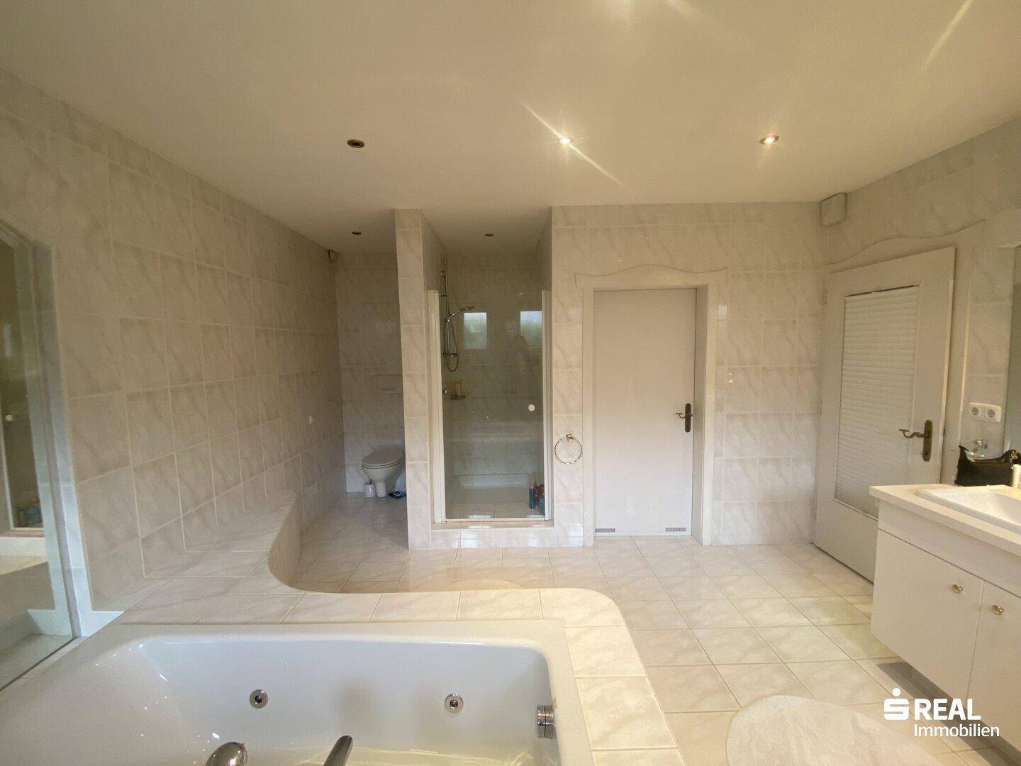 Geräumiges Badezimmer mit hellen Fliesen, integrierter Whirlpool-Badewanne und separater Dusche.
