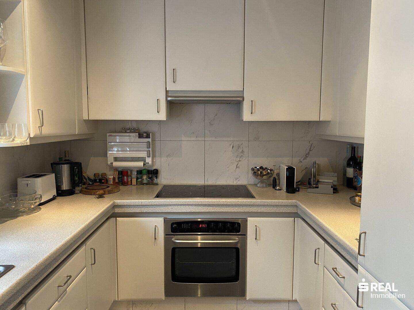 Funktionale Küche mit weißen Schränken, integriertem Backofen und moderner Kochfläche.