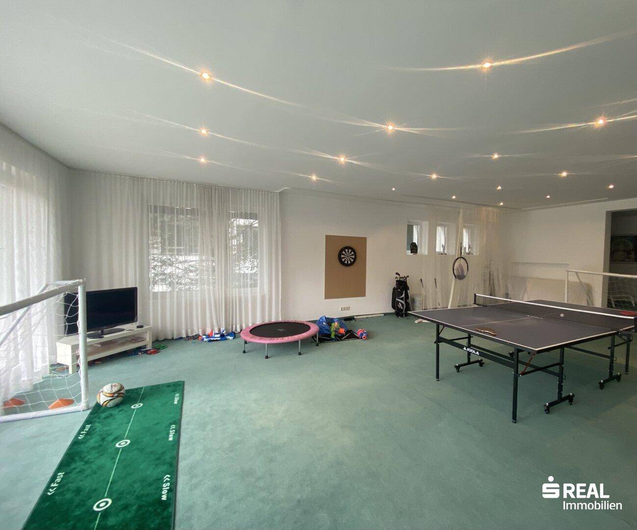 Vielseitiger Spielraum mit Tischtennisplatte, Dartscheibe und weiteren Sportgeräten für Unterhaltung.
