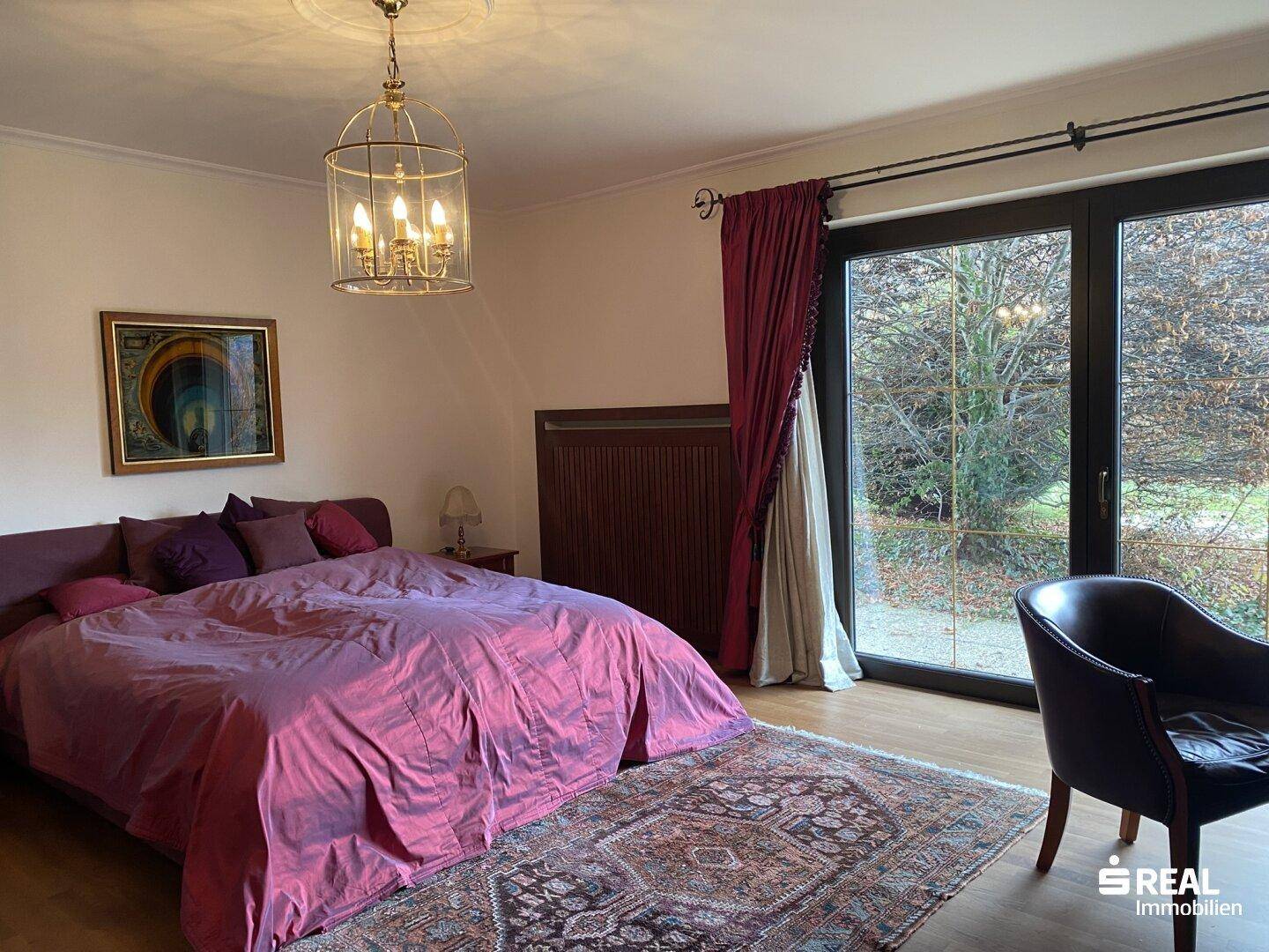 Helles Schlafzimmer mit Holzboden und großen Fenstern, die direkten Zugang zum Garten bieten.