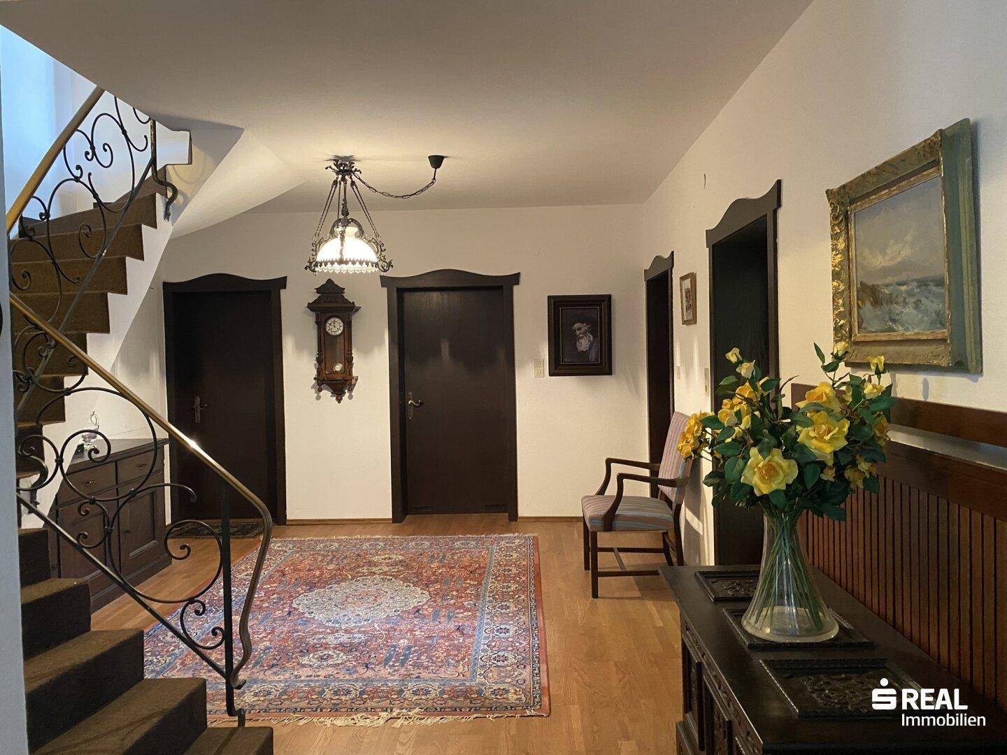 Geräumiger Eingangsbereich mit Holztreppe, traditionellem Teppich und dekorativen Elementen.