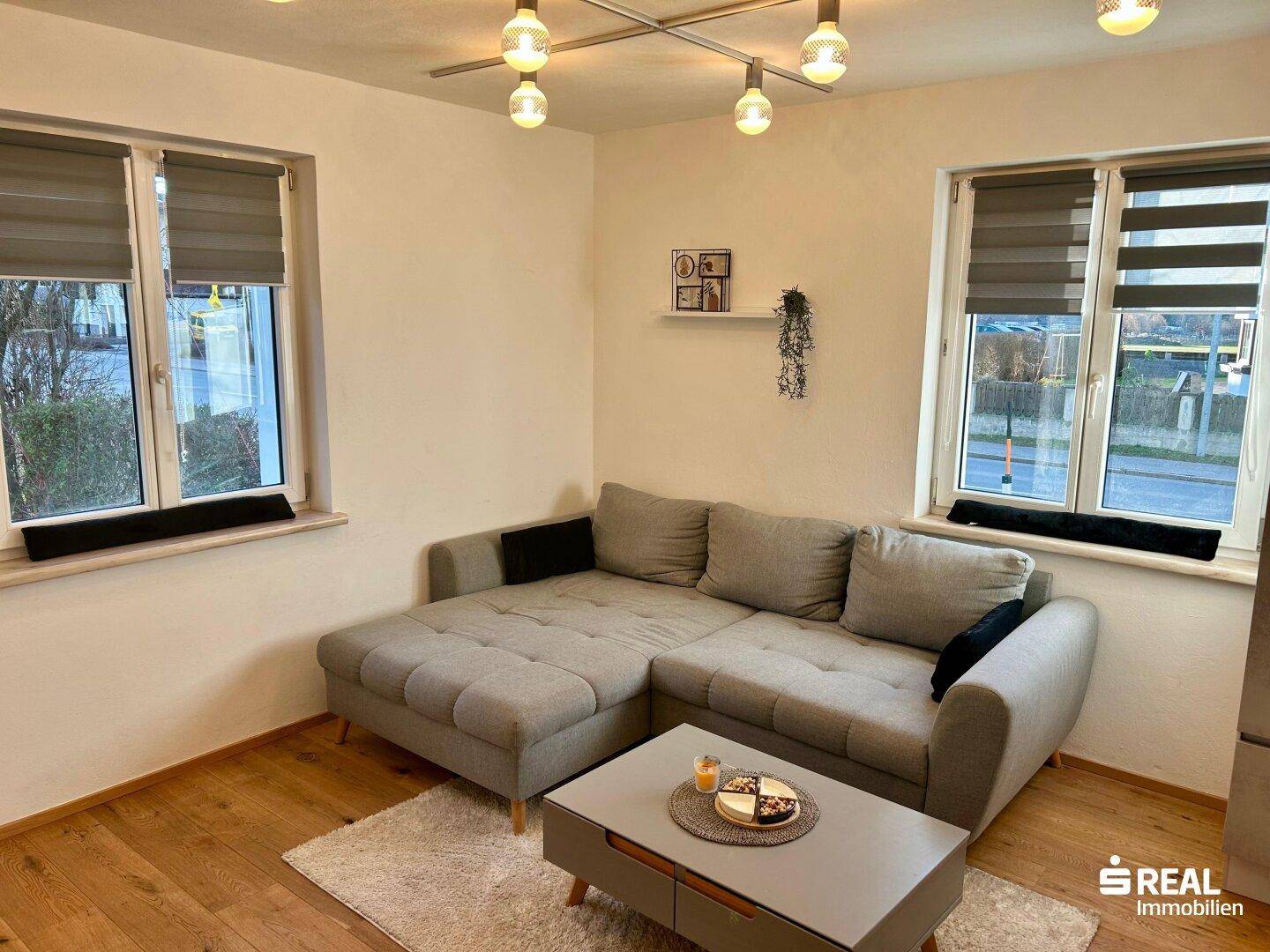 Heller Wohnbereich mit großem Ecksofa und Holzboden, ideal zum Entspannen und Verweilen.