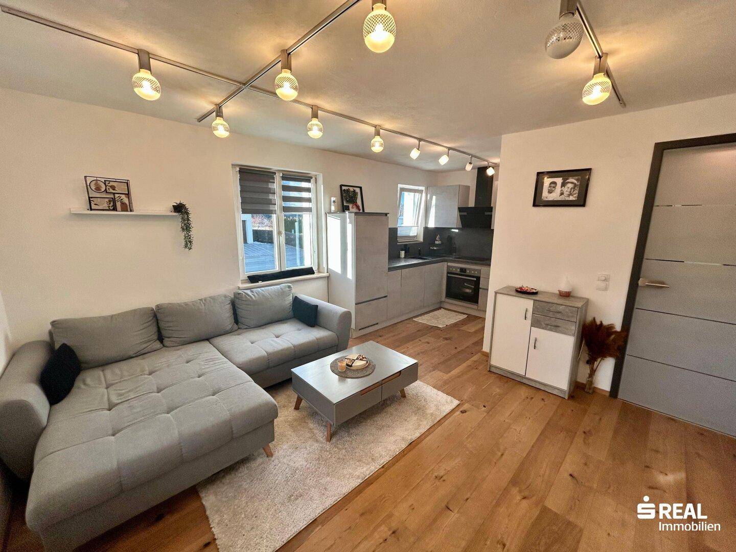 Gemütlicher Wohnbereich mit Ecksofa und Blick auf die offene Küche, ausgestattet mit modernen Geräten.
