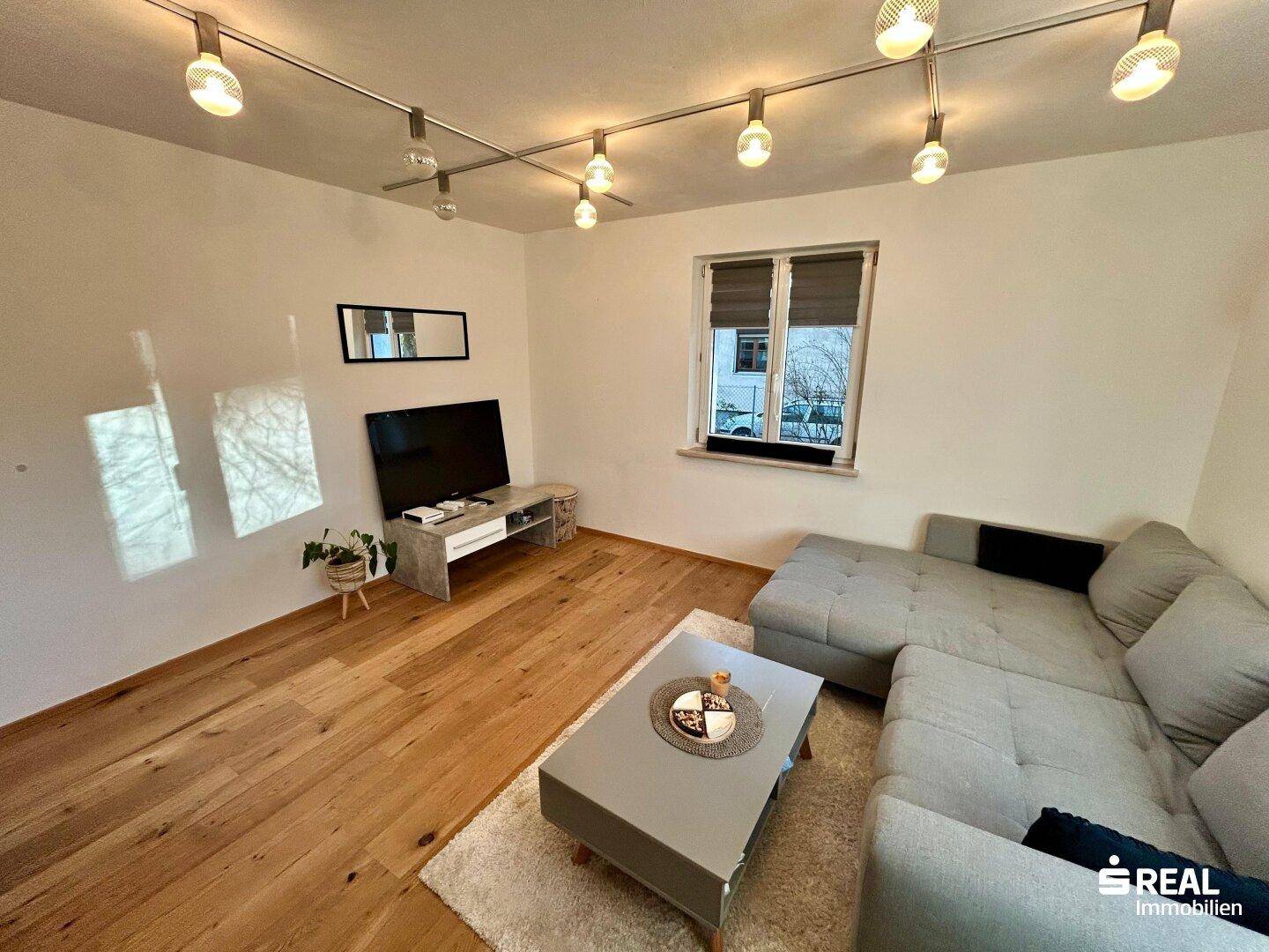 Geräumiger Wohnbereich mit Holzboden und TV-Möbel, bietet viel Platz für individuelle Gestaltung.