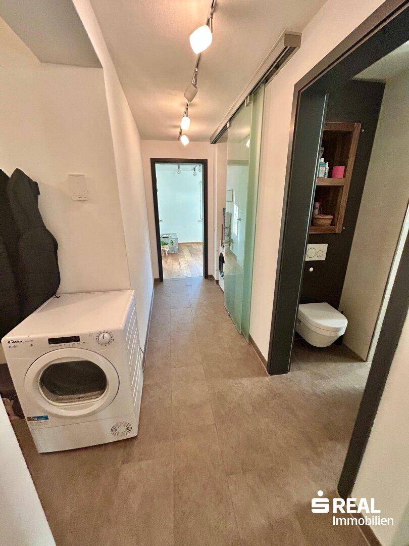 Langer Flur mit Fliesenboden und Waschmaschine, führt zu den weiteren Zimmern und dem WC.