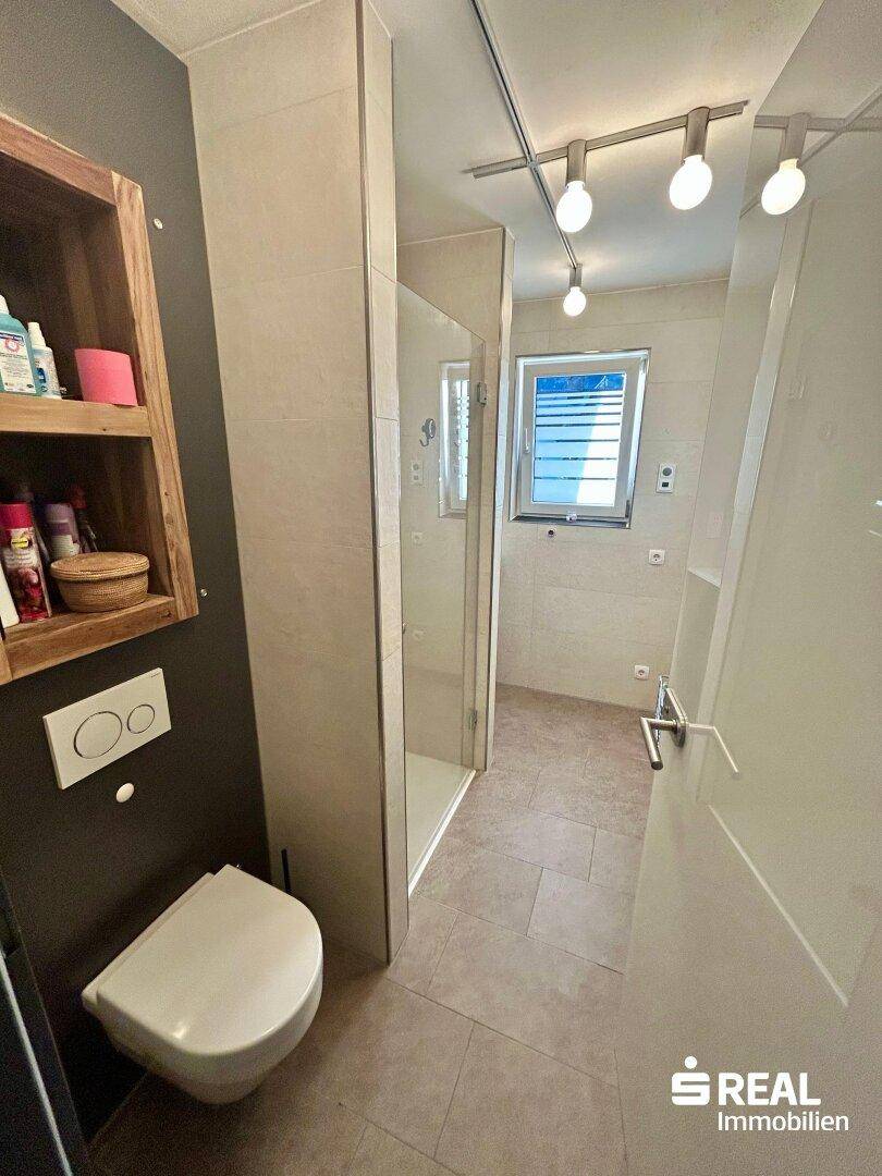 Modernes Badezimmer mit Fliesenboden, Duschkabine und wandhängendem WC, hell und funktional.