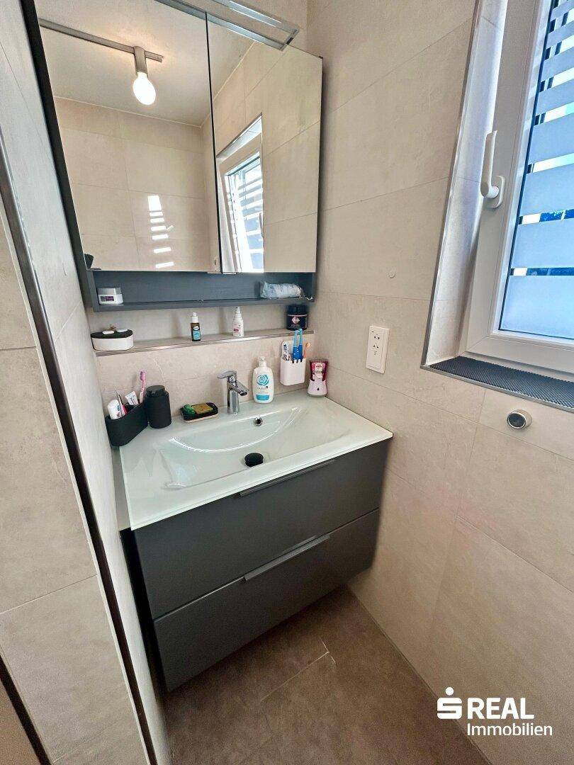 Modernes Badezimmer mit Waschtisch und Spiegelschrank, bietet praktischen Stauraum und viel Licht.