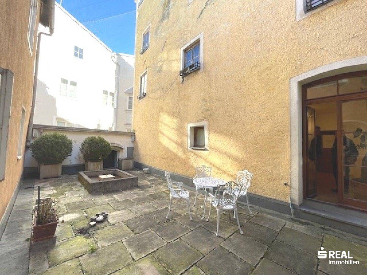 Sonniger Innenhof mit Steinfliesen und einer Tür, die in das Gebäude führt.