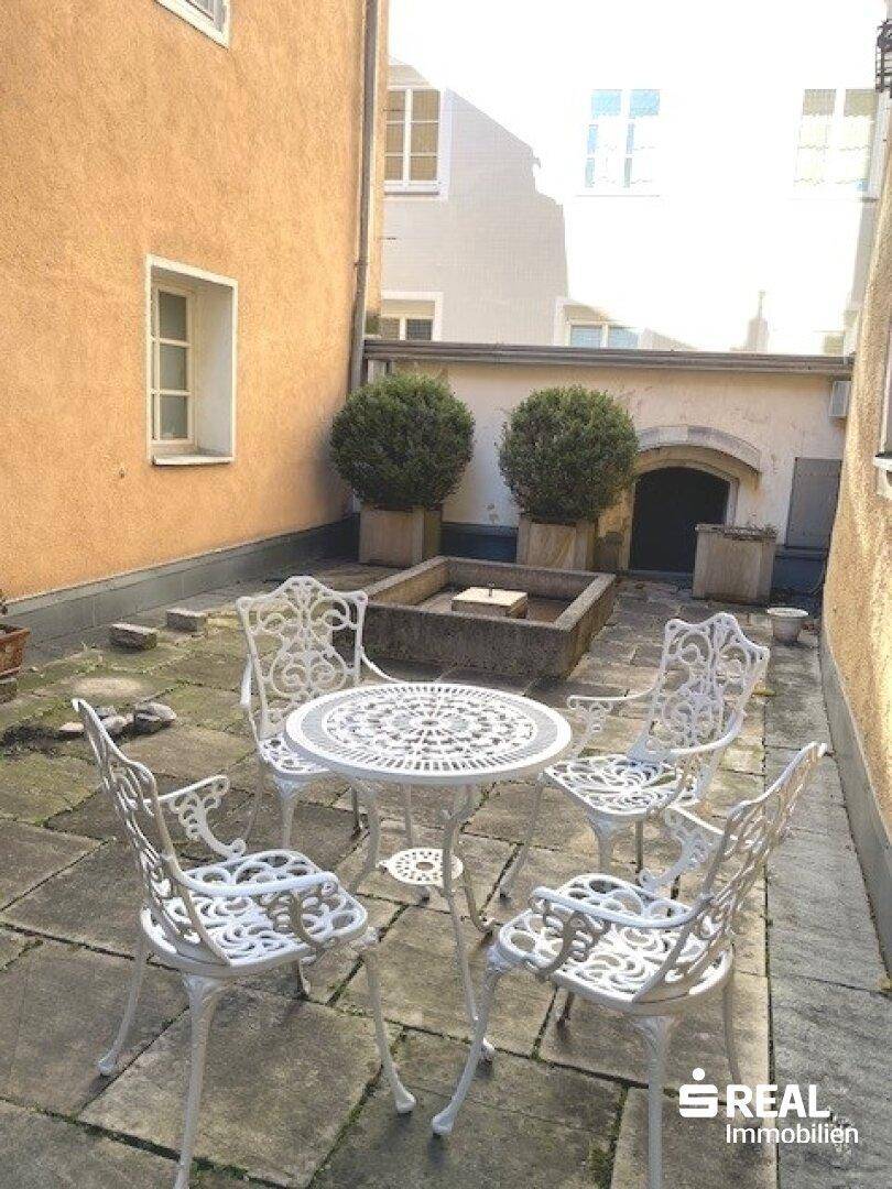 Ruhiger Innenhof mit Steinfliesen, Gartenmöbeln und grünen Pflanzen in Töpfen.