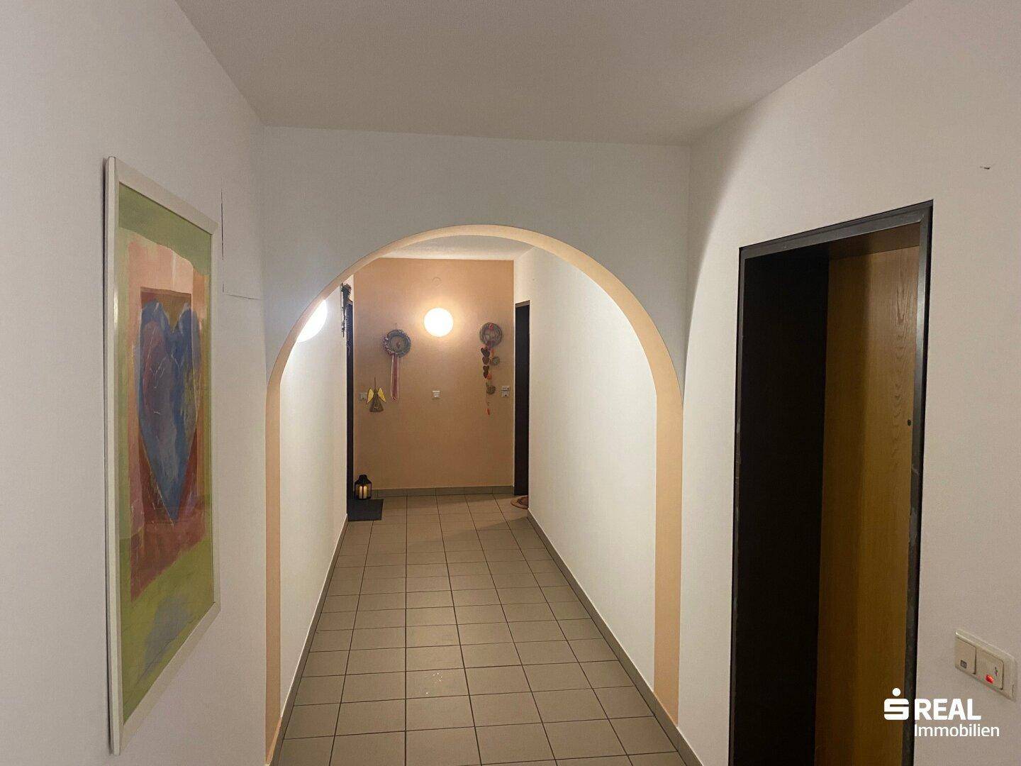 Heller Flur mit Fliesenboden und einem dekorativen Bogen, der zu weiteren Räumen führt.
