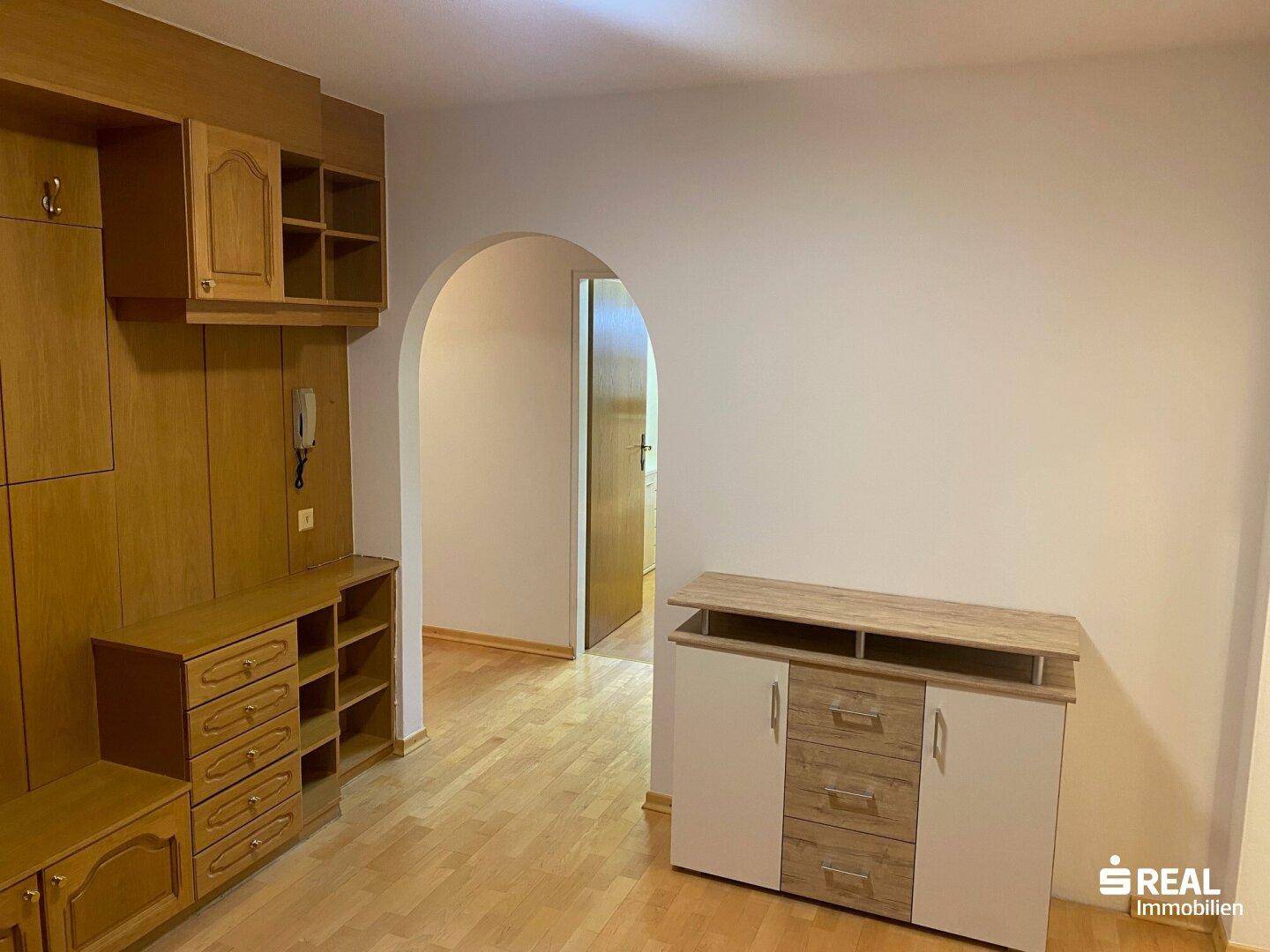 Eingangsbereich mit Holzmöbeln und einem Durchgang zu einem weiteren Raum mit Parkettboden.