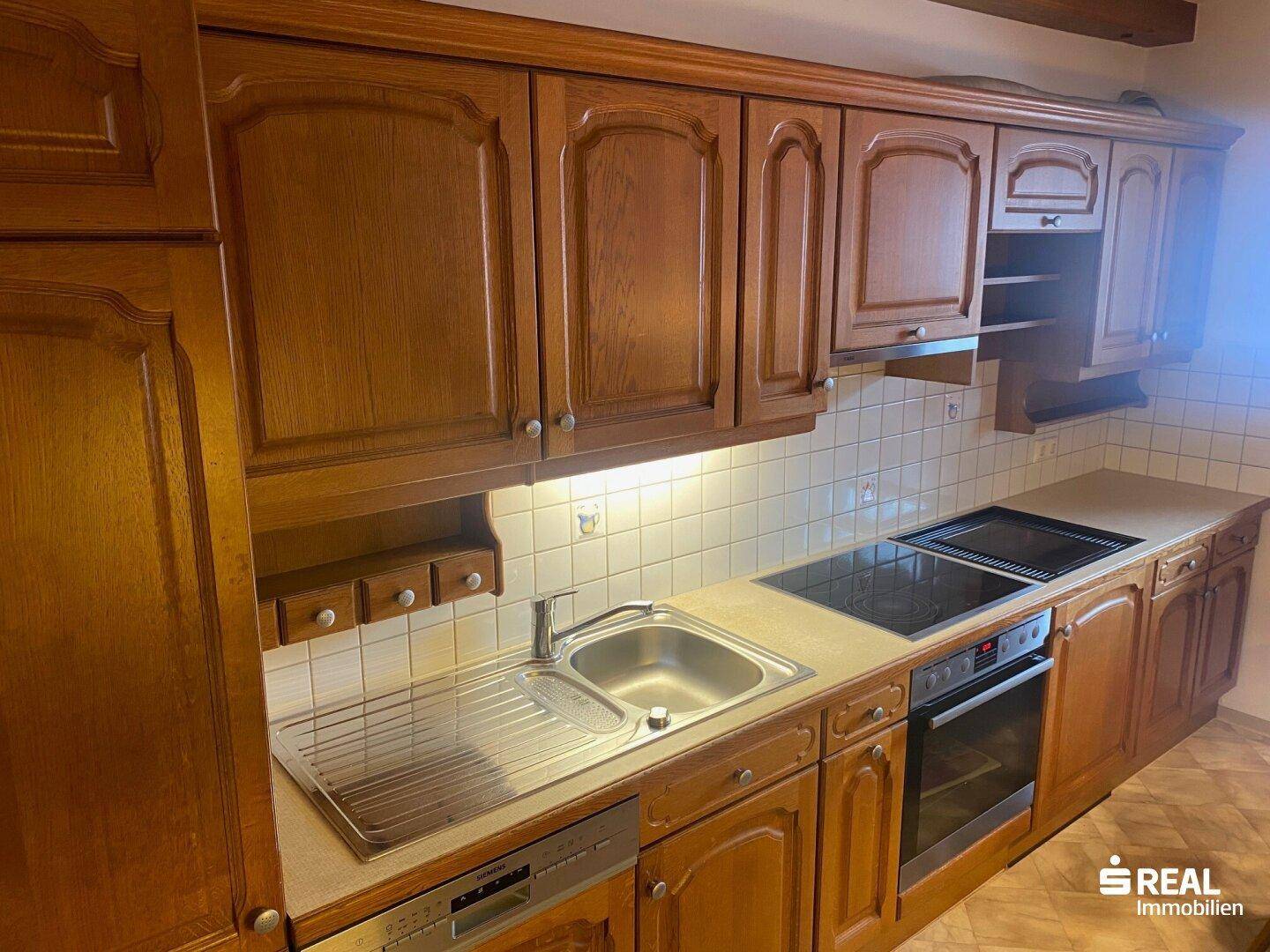 Detailansicht der Holzküche mit Spüle, Kochfeld und integriertem Geschirrspüler.