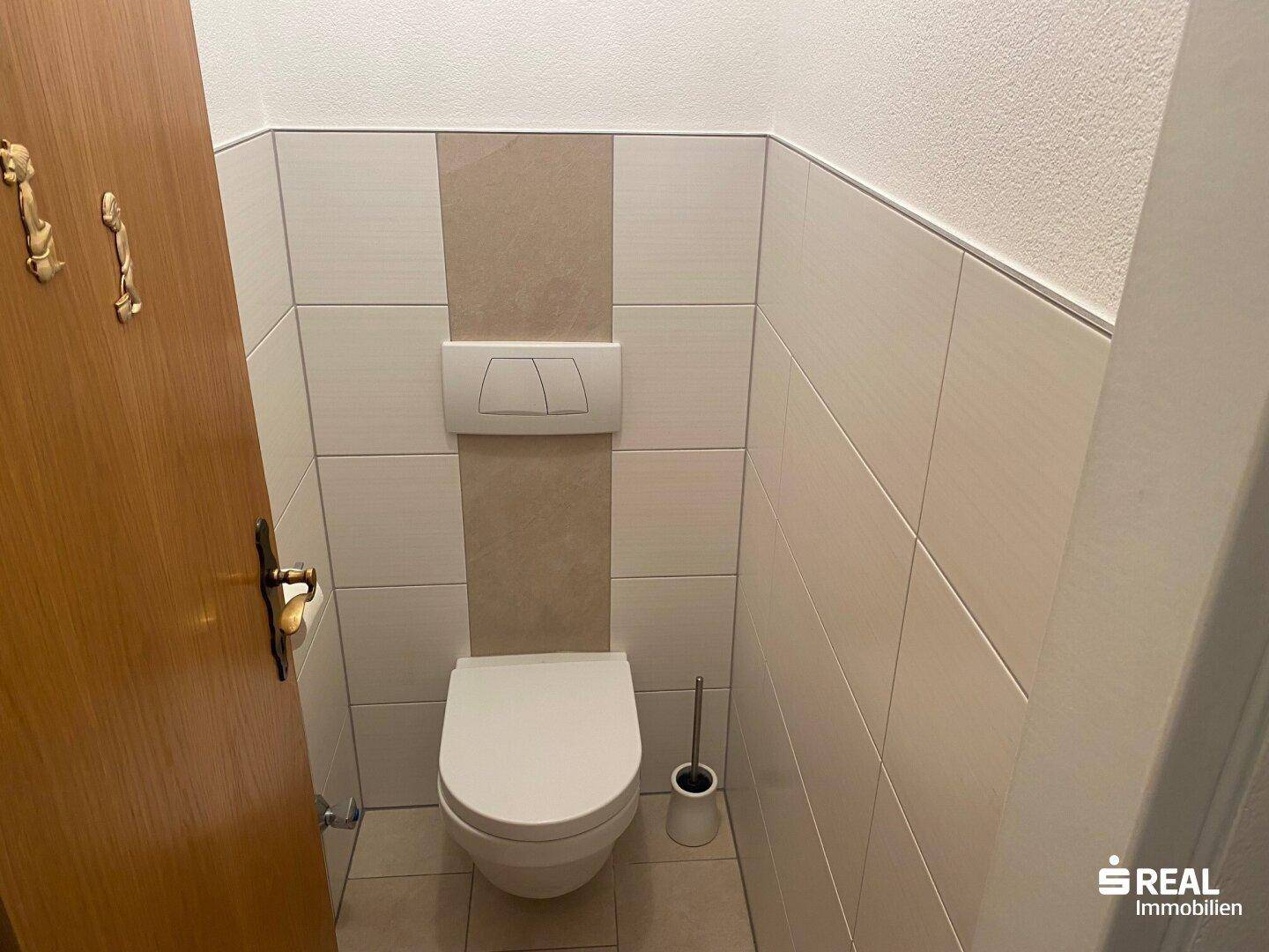 Separate Toilette mit Wand-WC und hellen Fliesen an den Wänden.