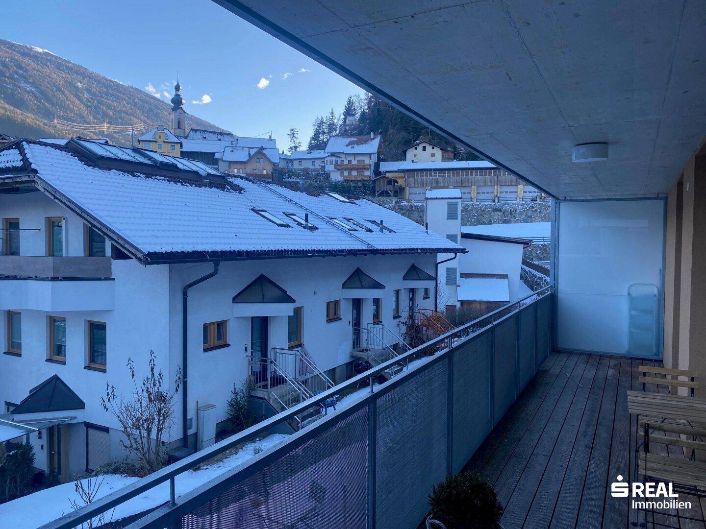 Großer Balkon mit Holzboden und weitem Blick auf schneebedeckte Häuser und Berge.
