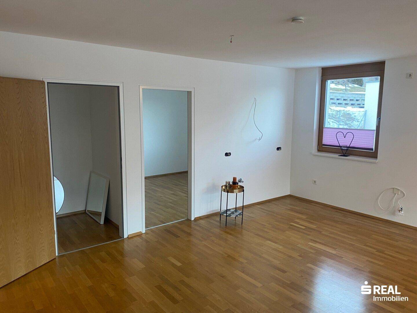Helles Zimmer mit Holzboden und offenen Türen zu angrenzenden Räumen.