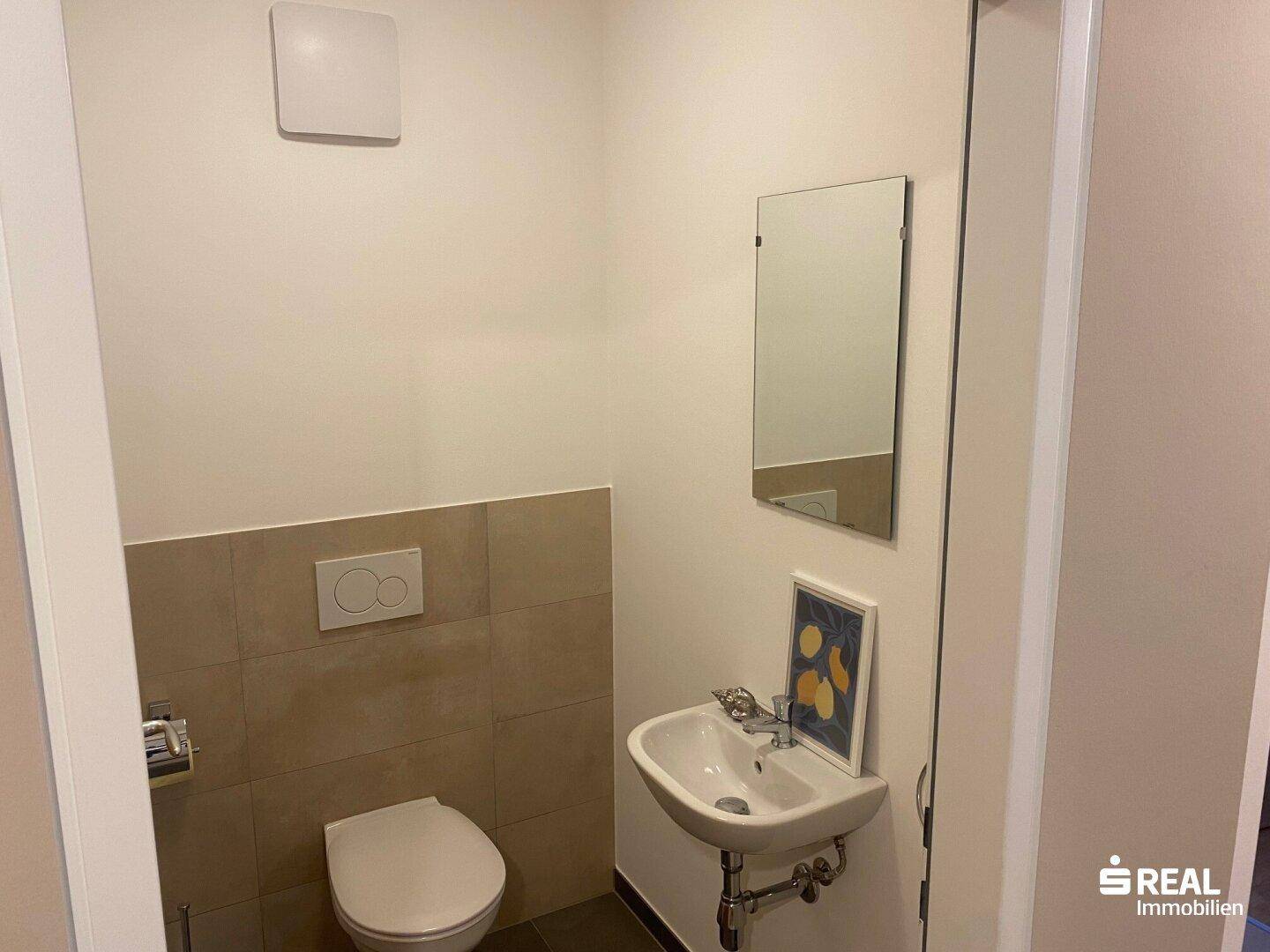 Separates Gäste-WC mit wandhängender Toilette, kleinem Waschbecken und Lüfter.