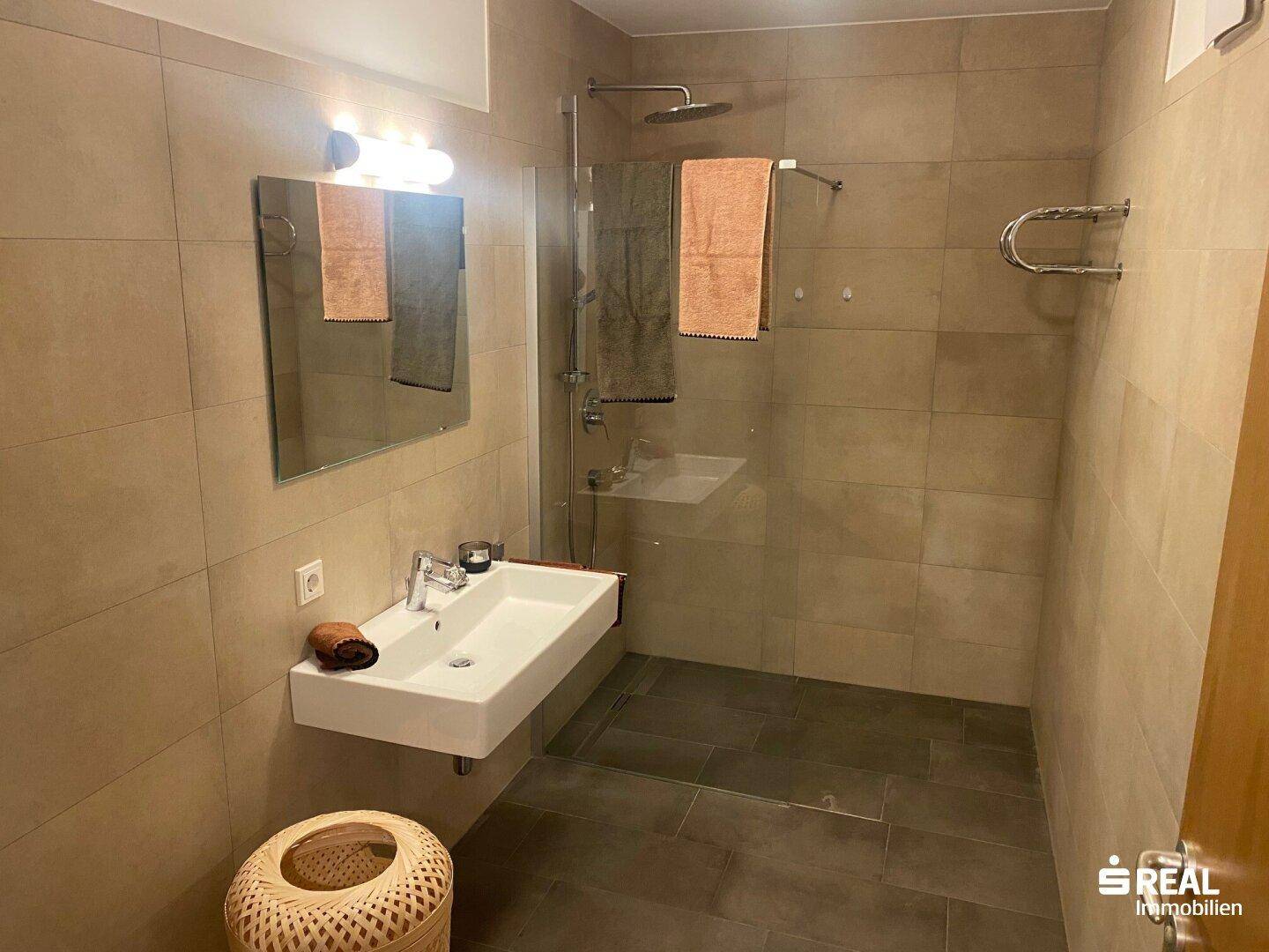 Modernes Badezimmer mit begehbarer Dusche, Wandwaschbecken und beigefarbenen Fliesen.