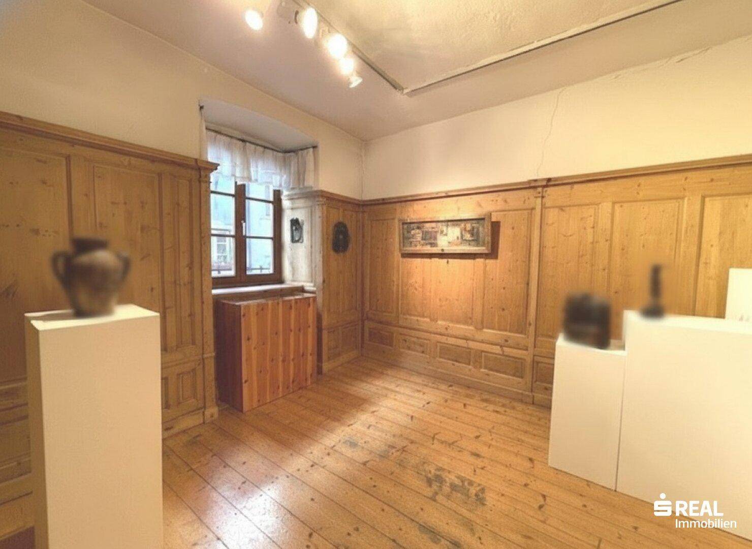 Traditioneller Raum mit Holztäfelung, Dielenboden und einem Fenster mit Vorhängen.