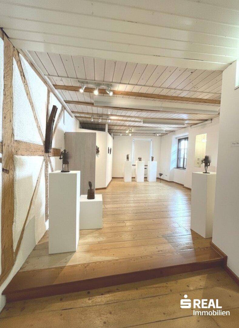 Geräumiger Raum mit Holzdielenboden, sichtbaren Deckenbalken und weiß getünchten Wänden.