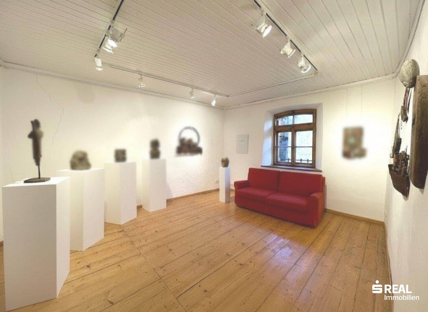 Heller Raum mit Holzdielenboden, weißer Decke und einem roten Sofa als Farbakzent.