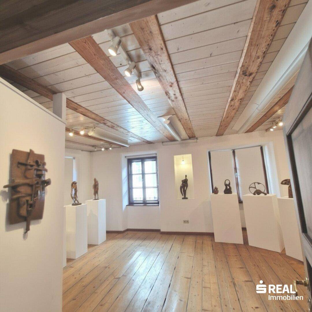 Heller Raum mit Holzdielenboden, sichtbaren Deckenbalken und Kunstobjekten.