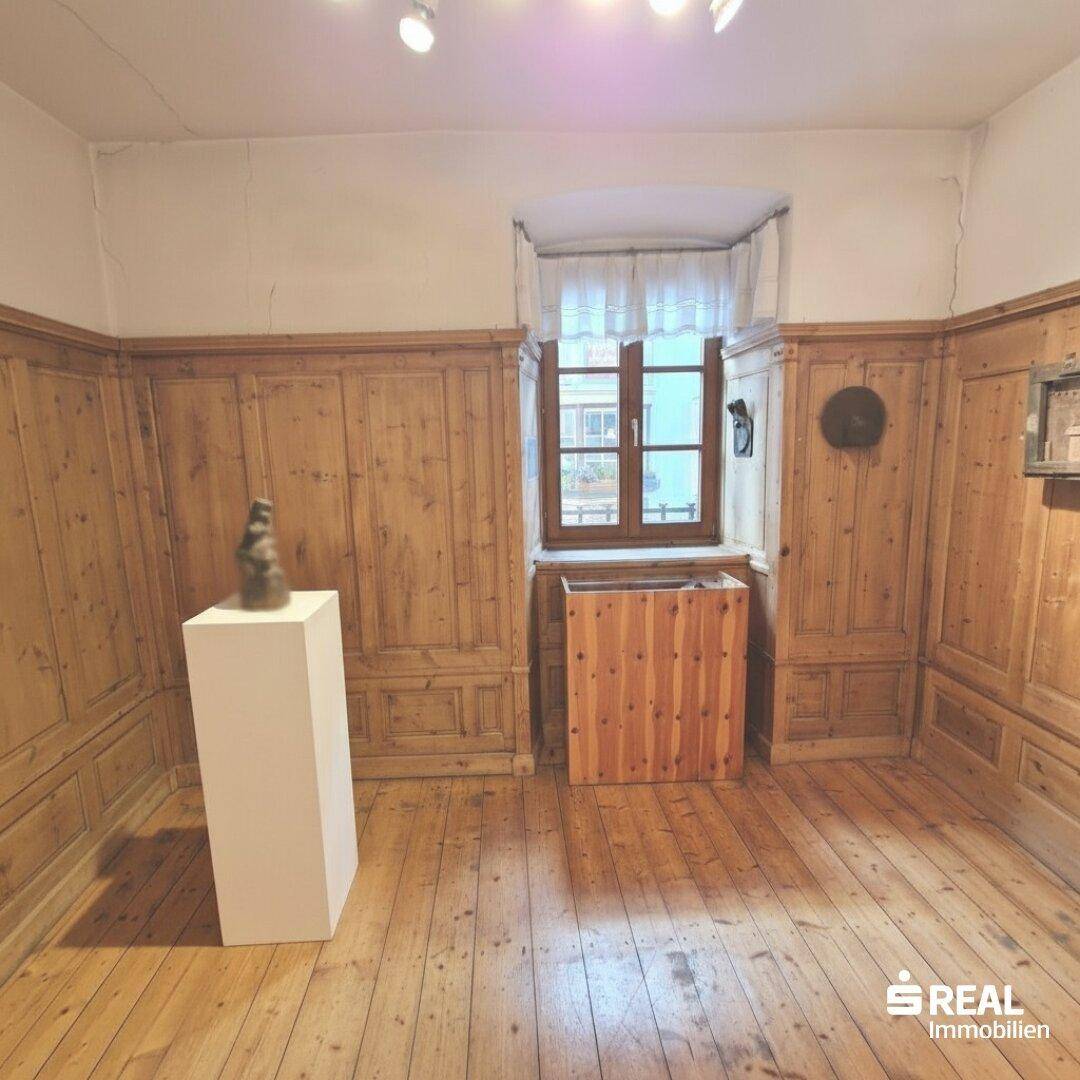 Traditioneller Raum mit Holztäfelung, Dielenboden und einem Fenster mit Vorhängen.
