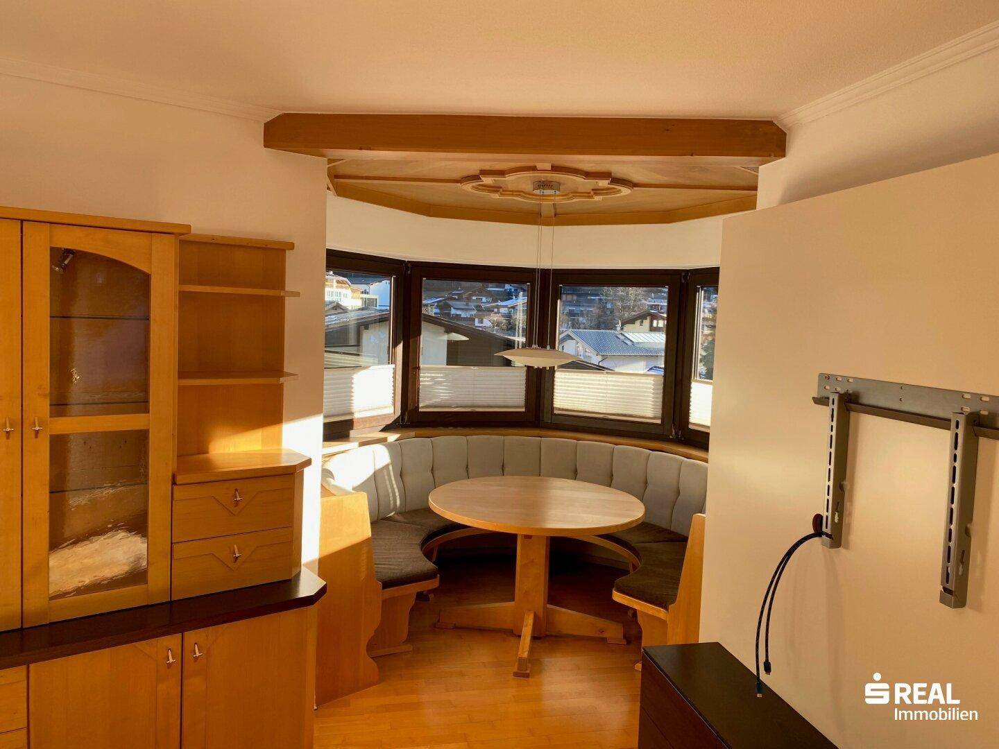 Gemütlicher Essbereich mit Holztisch, Eckbank und großen Fenstern, die viel Tageslicht hereinlassen.