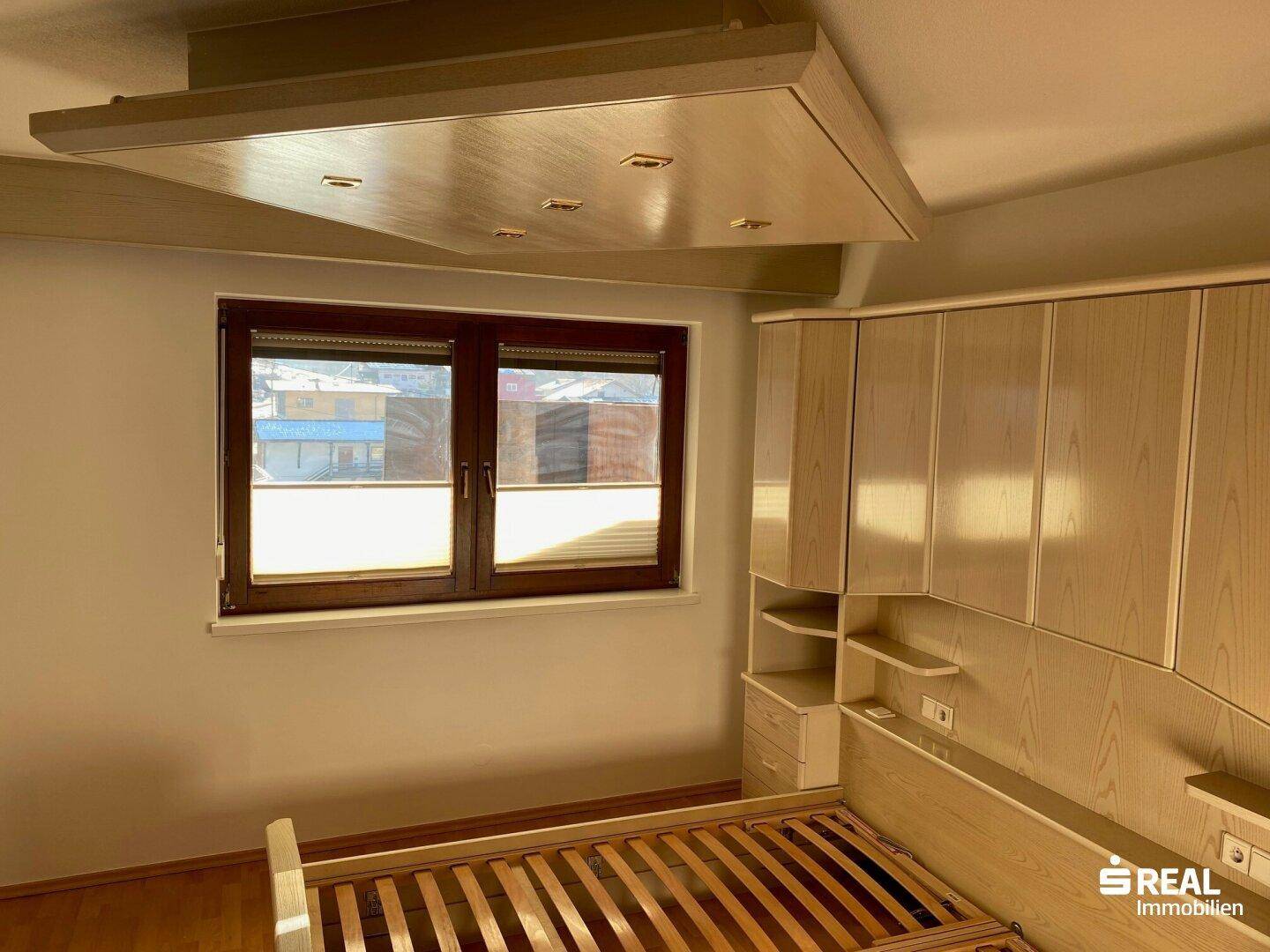 Helles Schlafzimmer mit integrierten Kleiderschränken und einem Fenster mit Rollladen.