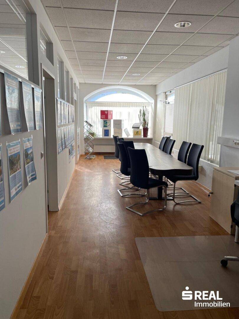Geräumiger Konferenzraum mit langem Tisch, schwarzen Stühlen und natürlichem Lichteinfall durch Fenster.