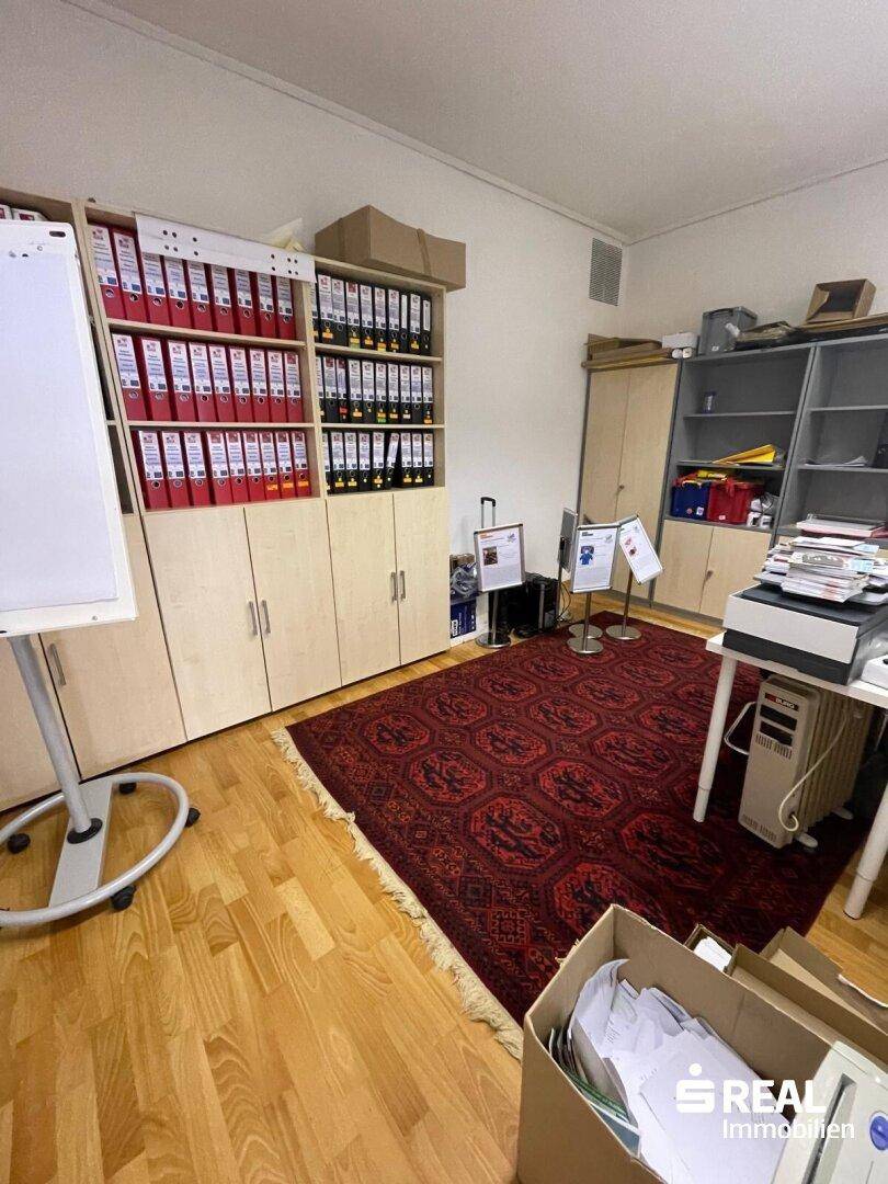 Bürobereich mit Aktenschränken, einem roten Teppich und einem Drucker auf einem Beistelltisch.
