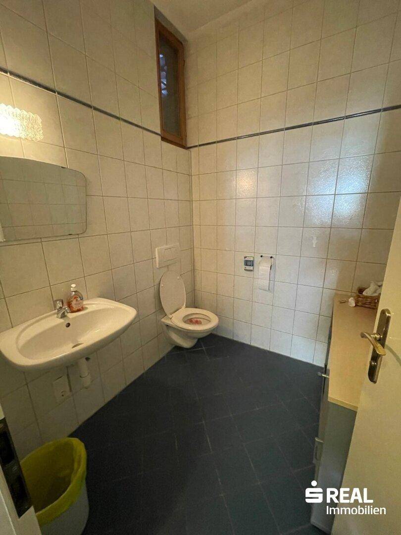 Gefliestes Badezimmer mit WC, Waschbecken und einem kleinen Fenster für Belüftung.
