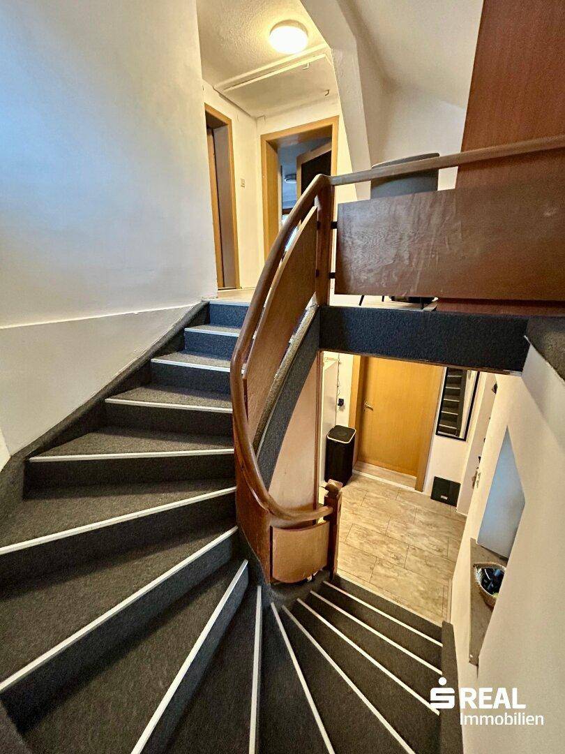 Wendeltreppe mit dunklem Teppichbelag und elegantem Holzgeländer, die die Etagen verbindet.
