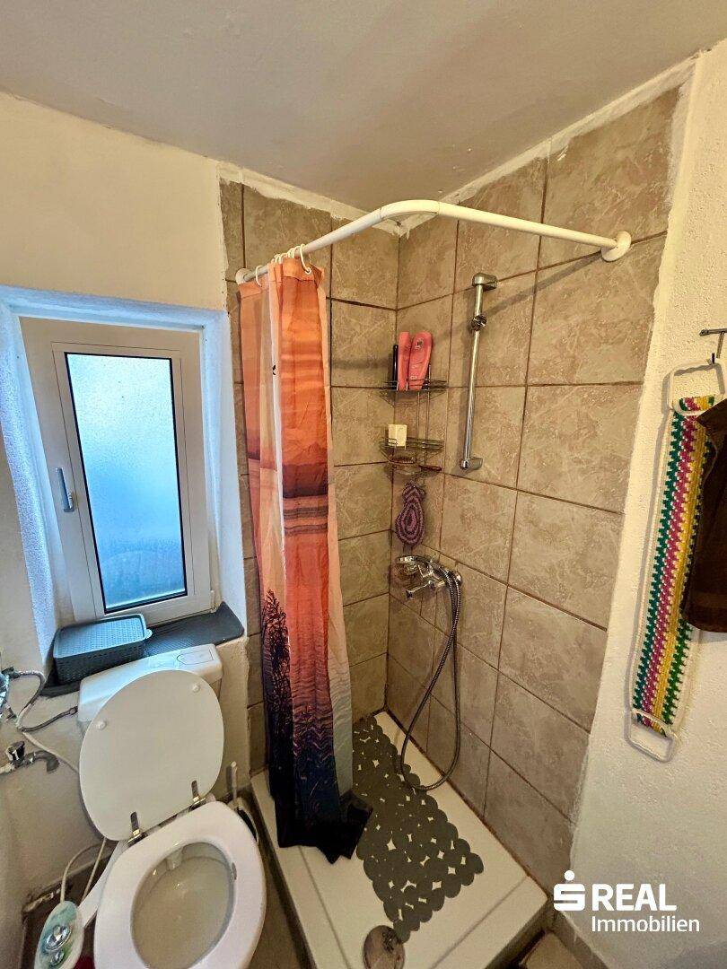 Badezimmer mit Toilette, Duschbereich mit Vorhang und hellbraunen Wandfliesen.
