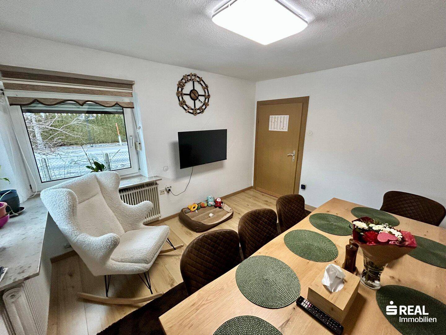Essbereich mit Fernseher, Holztisch und Blick auf den Außenbereich durch das Fenster.