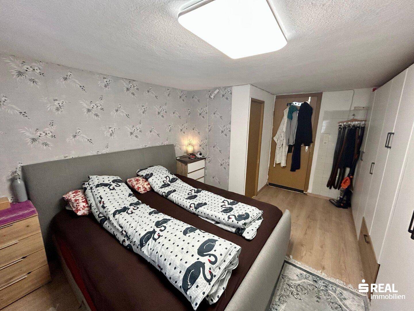 Schlafzimmer mit Doppelbett, gemusterter Tapete und praktischen weißen Kleiderschränken.