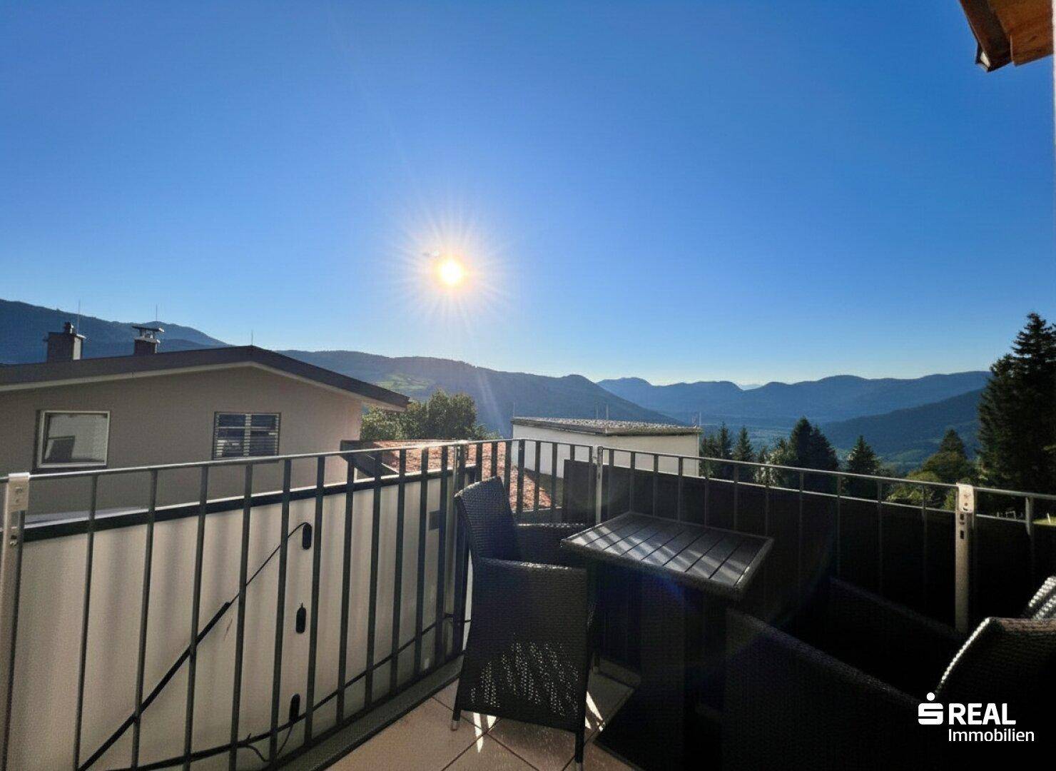 Sonniger Balkon mit Sitzgelegenheiten und weitem Blick auf die Berge.
