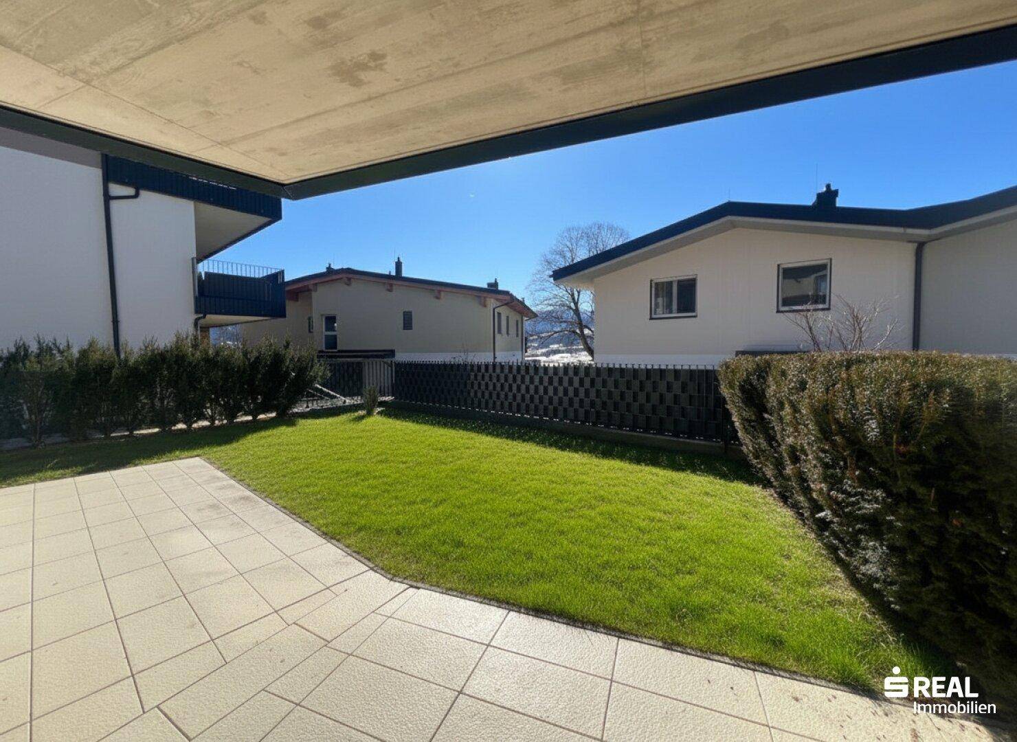 Gepflegter Gartenbereich mit Rasenfläche und gepflasterter Terrasse.