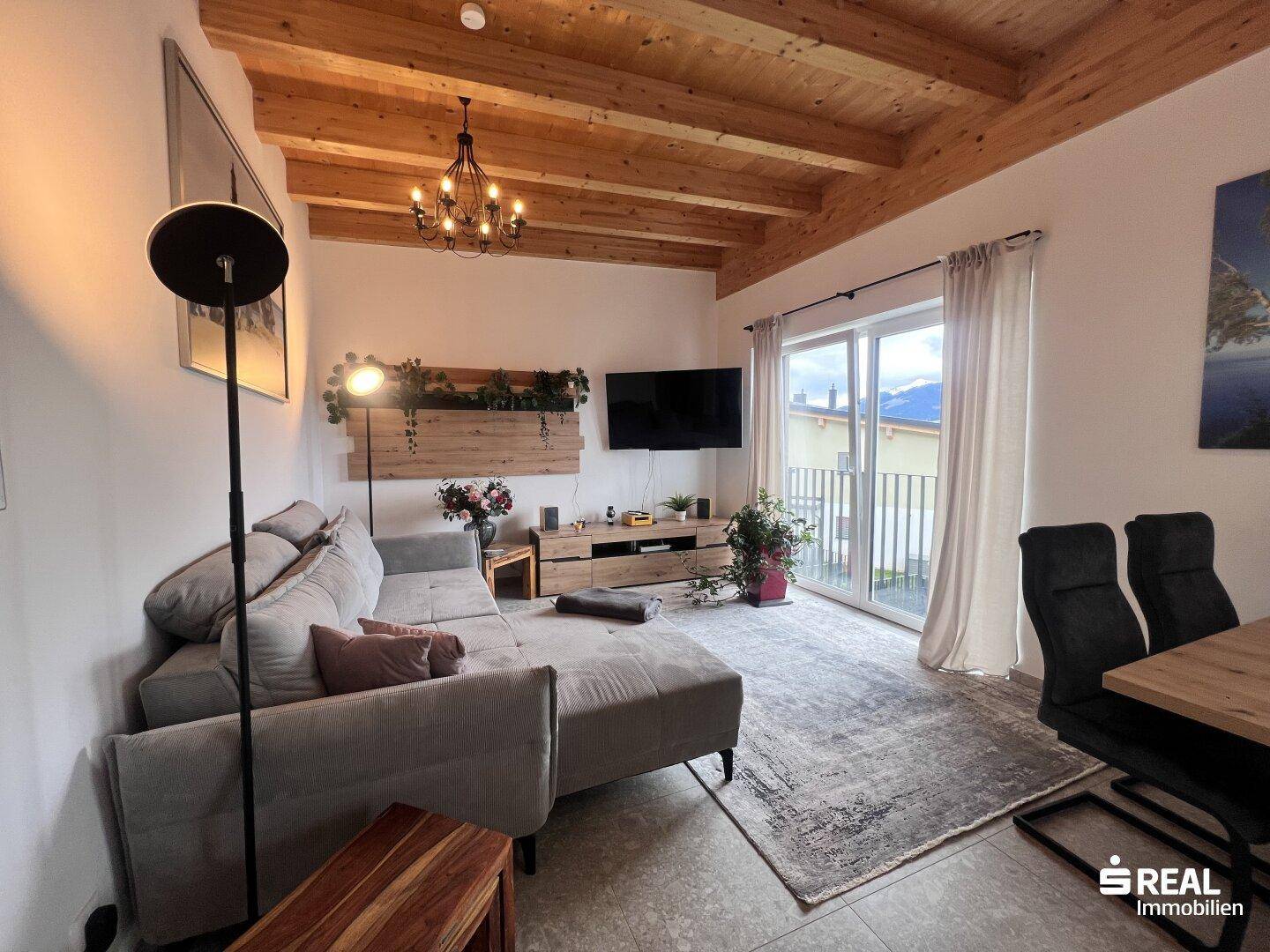 Gemütlicher Wohnbereich mit Holzbalkendecke, Sofa und Zugang zum Balkon.