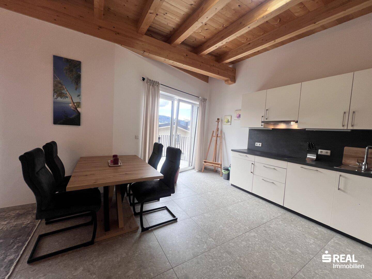 Offene Küche mit Esstisch, weißen Schränken und Holzbalkendecke.