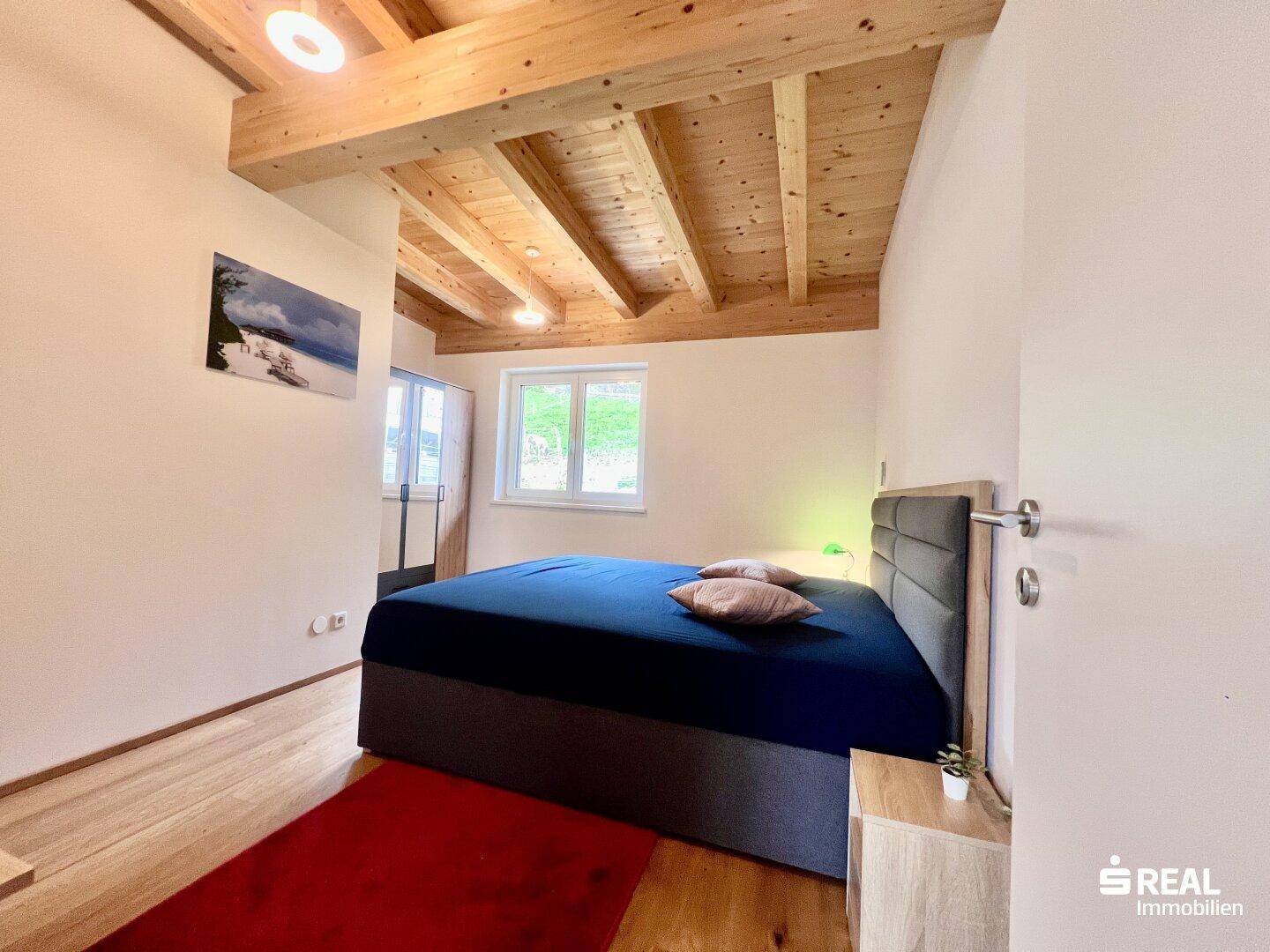 Schlafzimmer mit Holzbalkendecke, Holzboden und großem Bett.