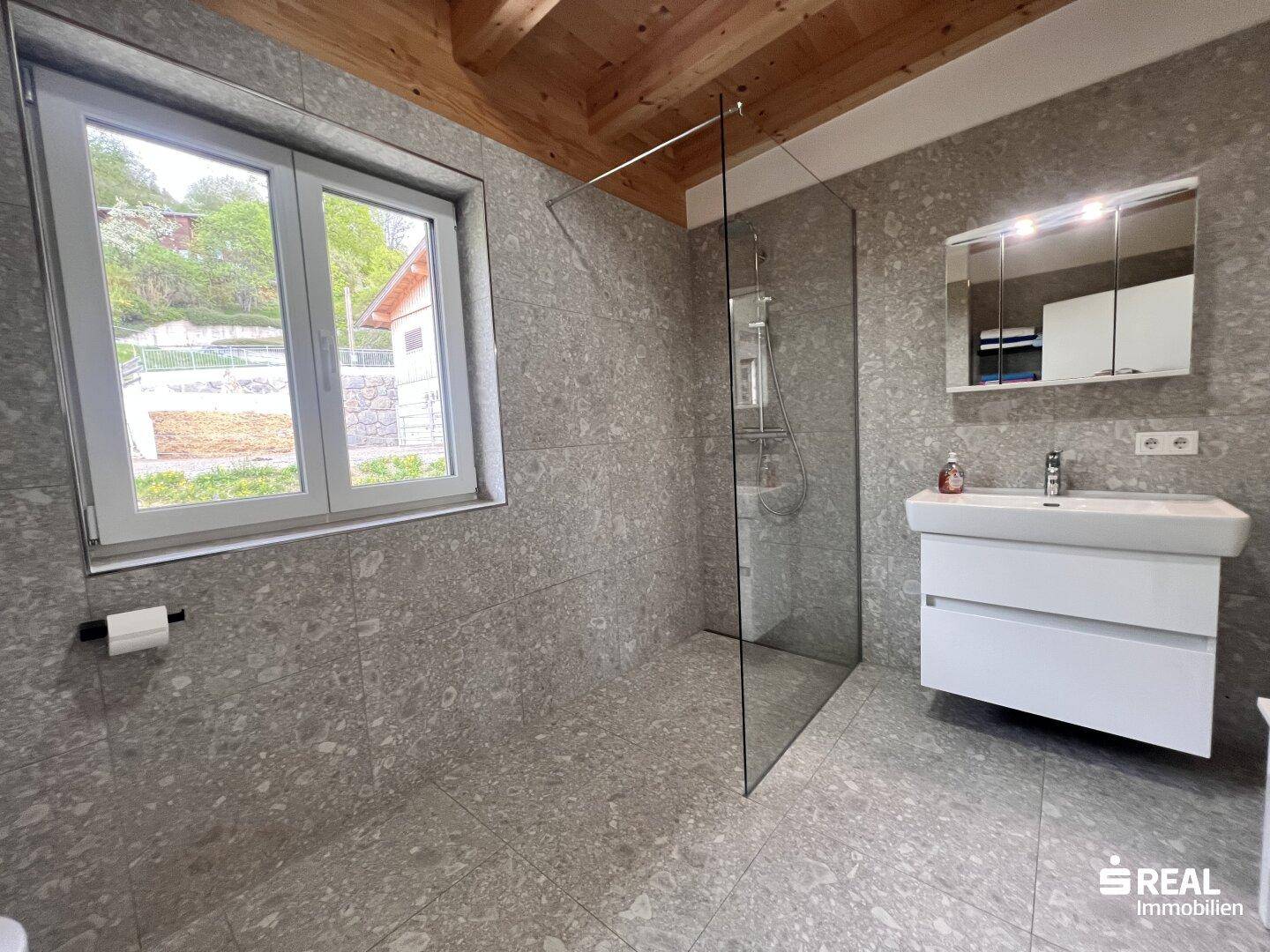 Modernes Badezimmer mit großer begehbarer Dusche, Fenster und grauen Fliesen.